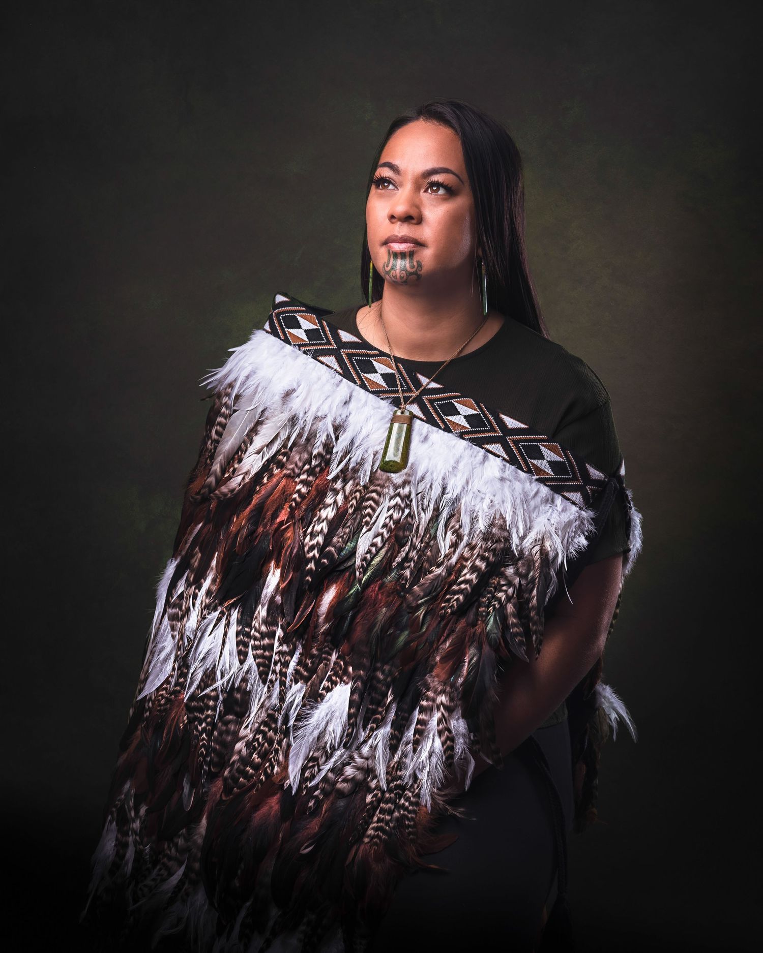 Portrait against dark background showing traditional Indigenous regalia with feathers and geometric patterns.