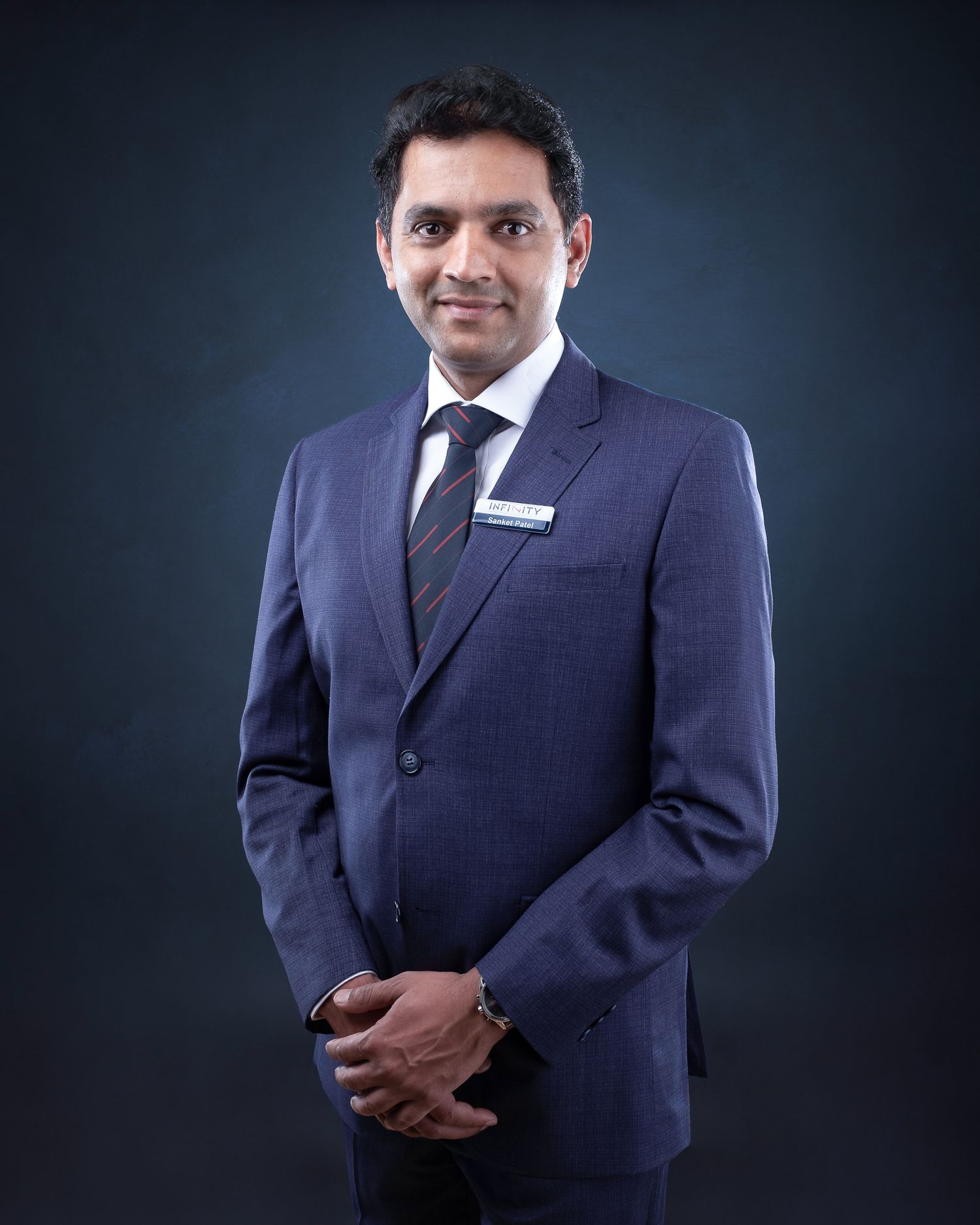 Professional business portrait of person in dark navy suit with tie against dramatic studio backdrop.