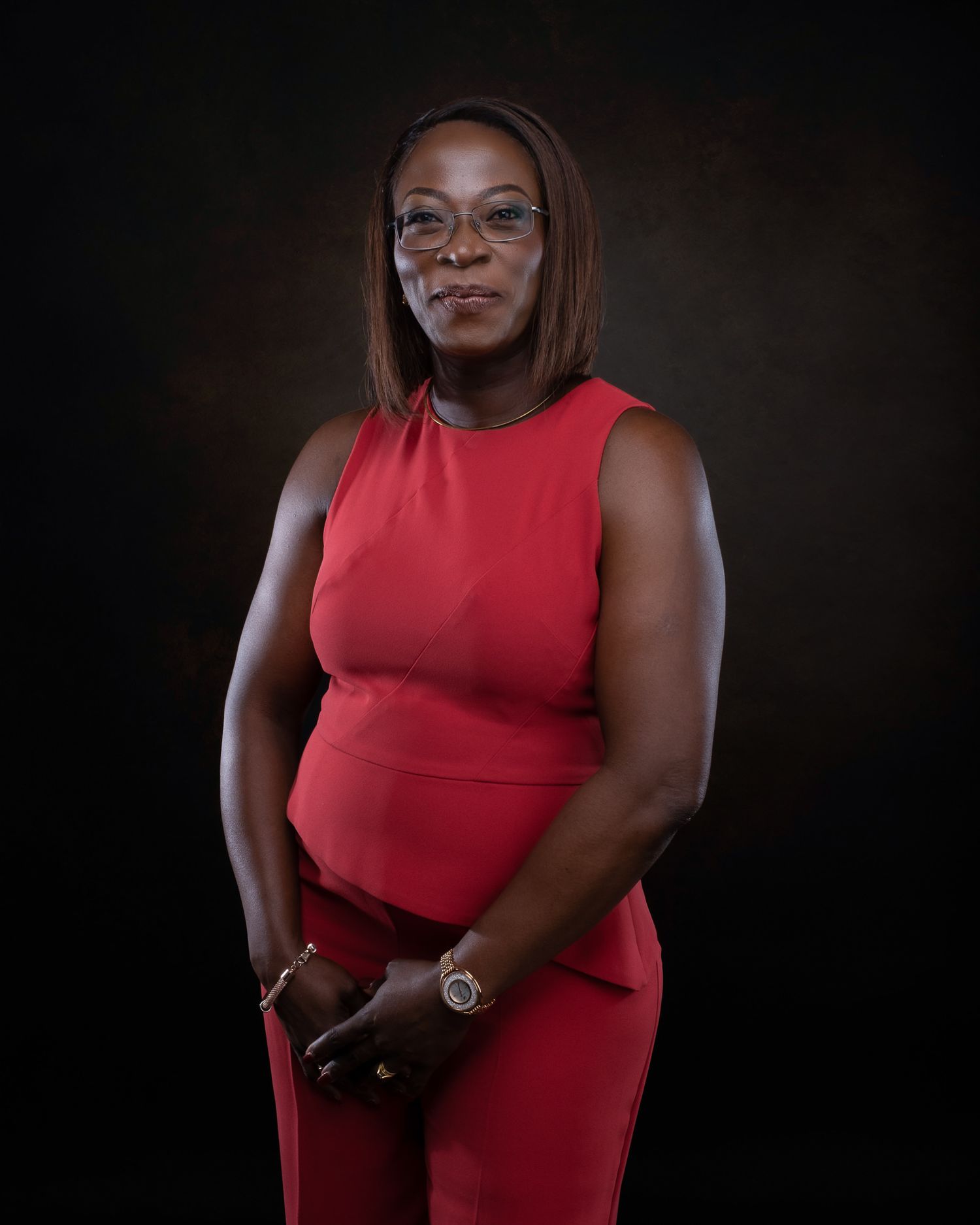 Professional portrait of person wearing sleeveless red dress against dark background.