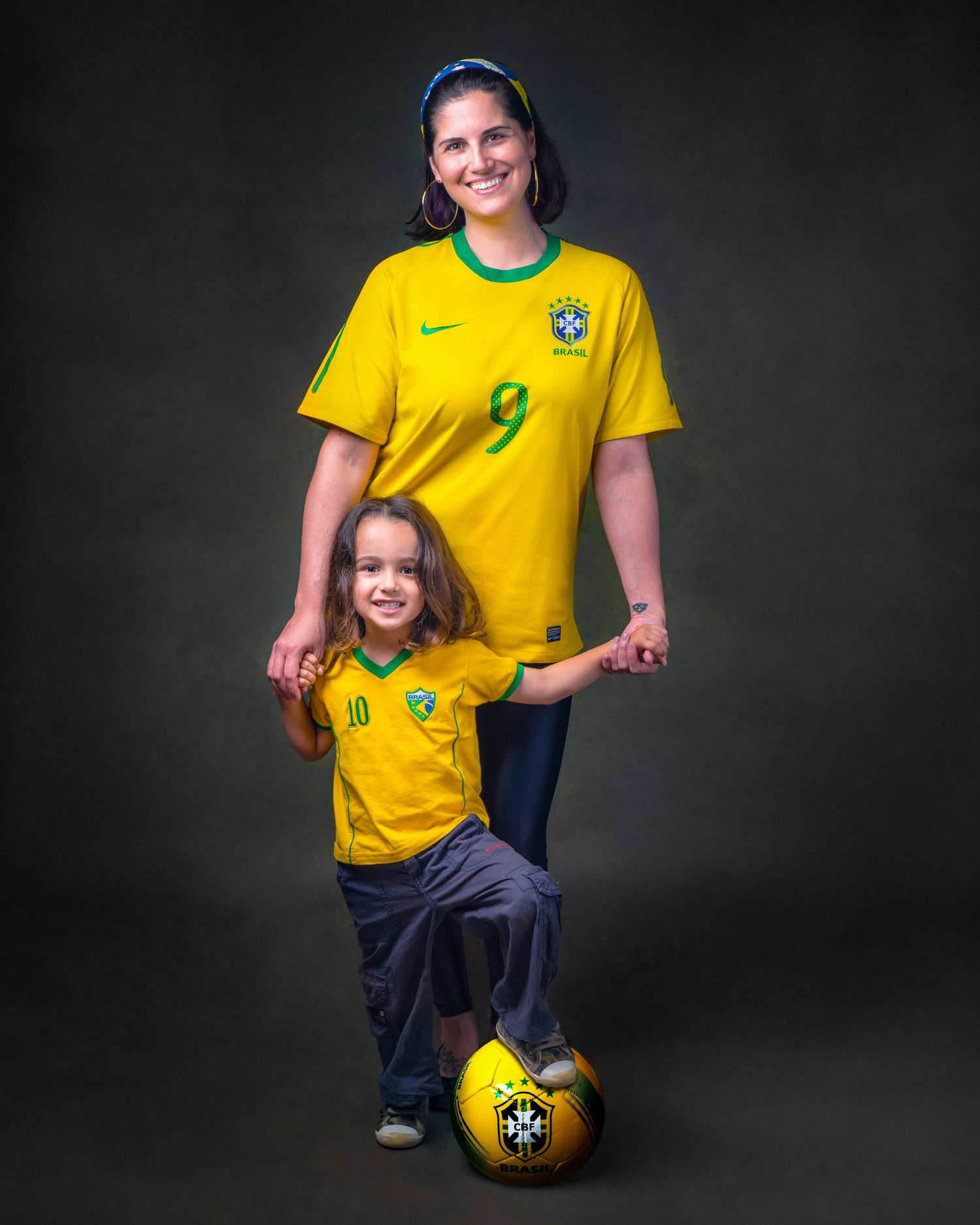 Soccer fans wearing Brazil national team jerseys pose with a soccer ball against a dark background in a studio portrait.