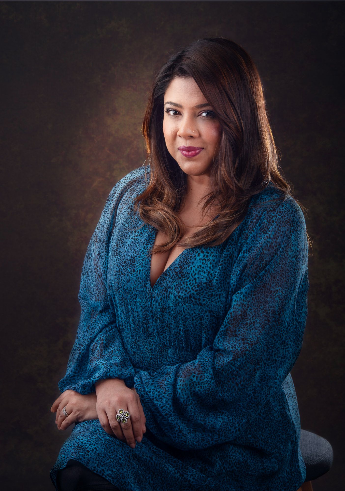 Studio portrait of a person in a shimmering teal blue sweater against a dark backdrop with dramatic lighting.