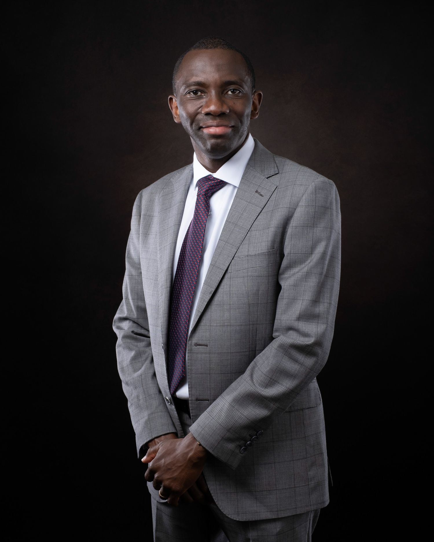 Professional portrait of someone wearing a gray suit and purple tie against a dark background.