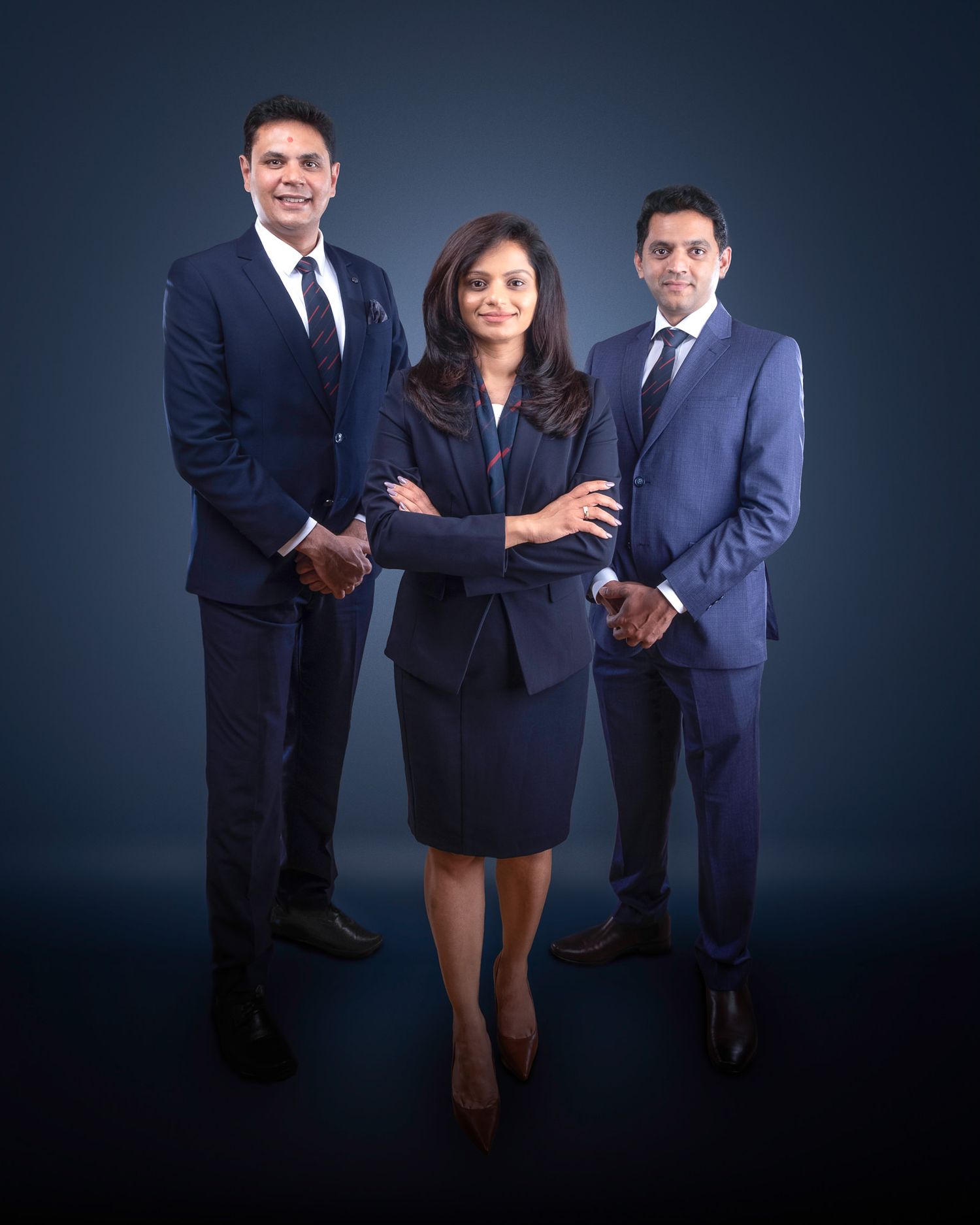 Three business professionals in dark suits pose confidently against a navy blue background for a corporate portrait.