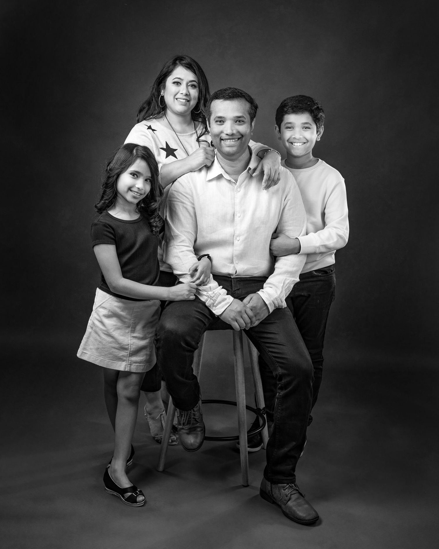 Timeless black and white portrait of a family of four against a dark background.