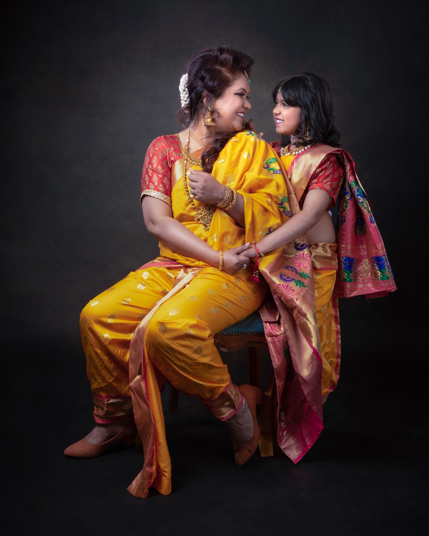 Two people in vibrant yellow and red traditional attire pose intimately against a dark backdrop in a studio setting.