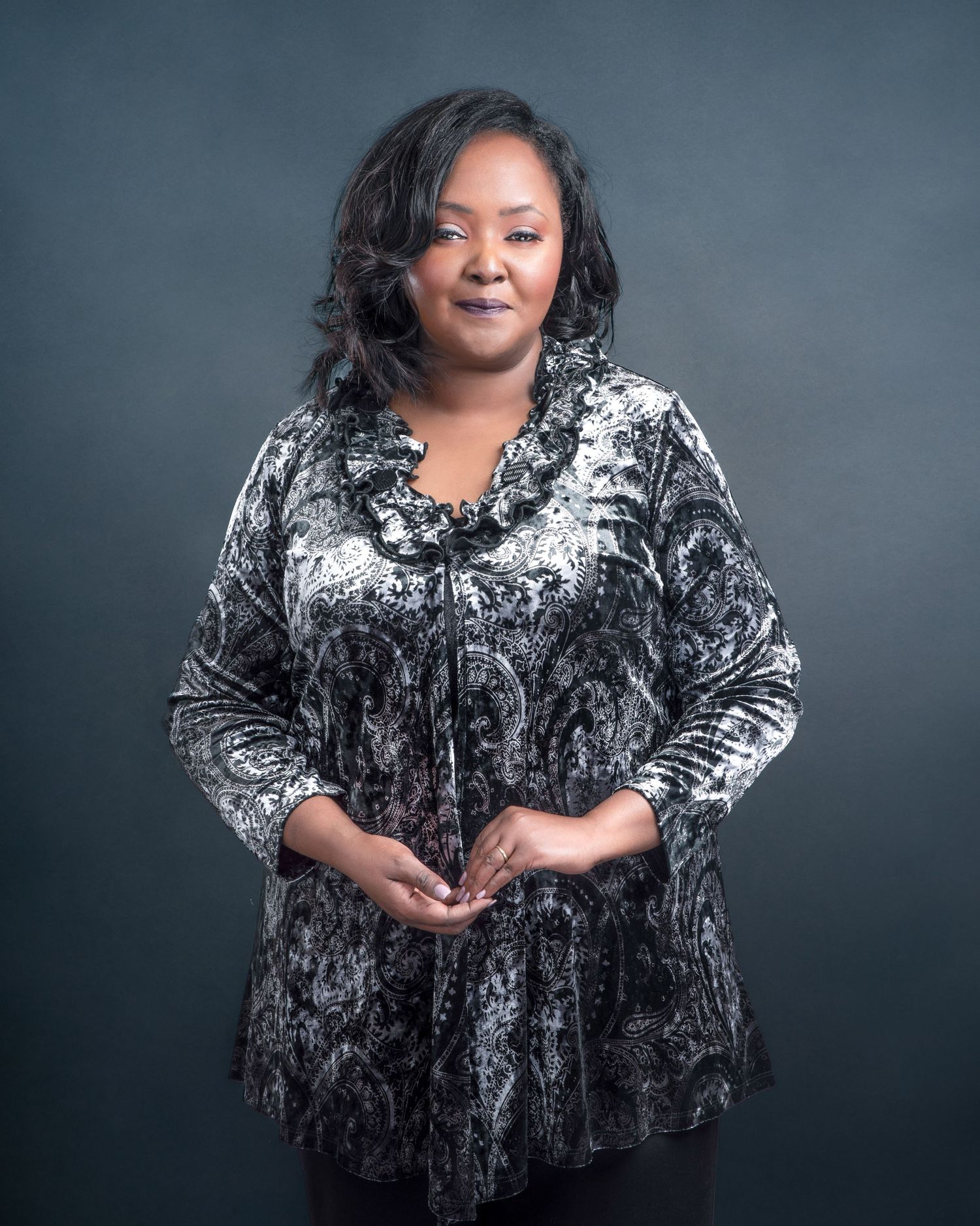 Studio portrait in black and grey tones featuring warm smile and crushed velvet tunic against a dark background.