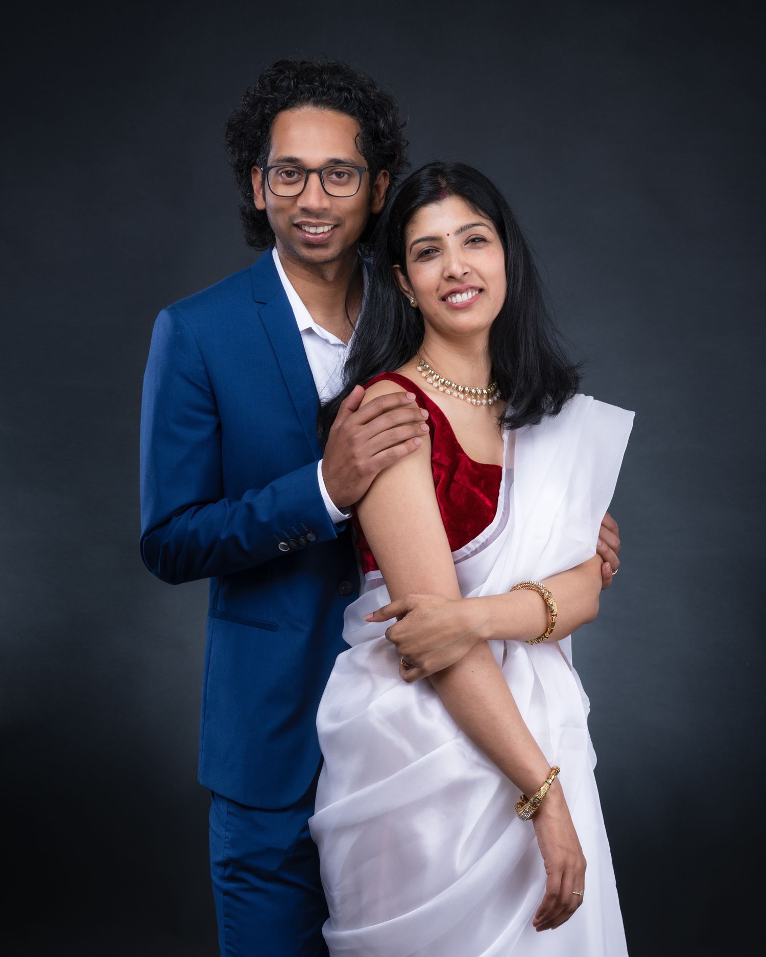 Professional studio portrait of a couple in formal attire embracing against a dark background.