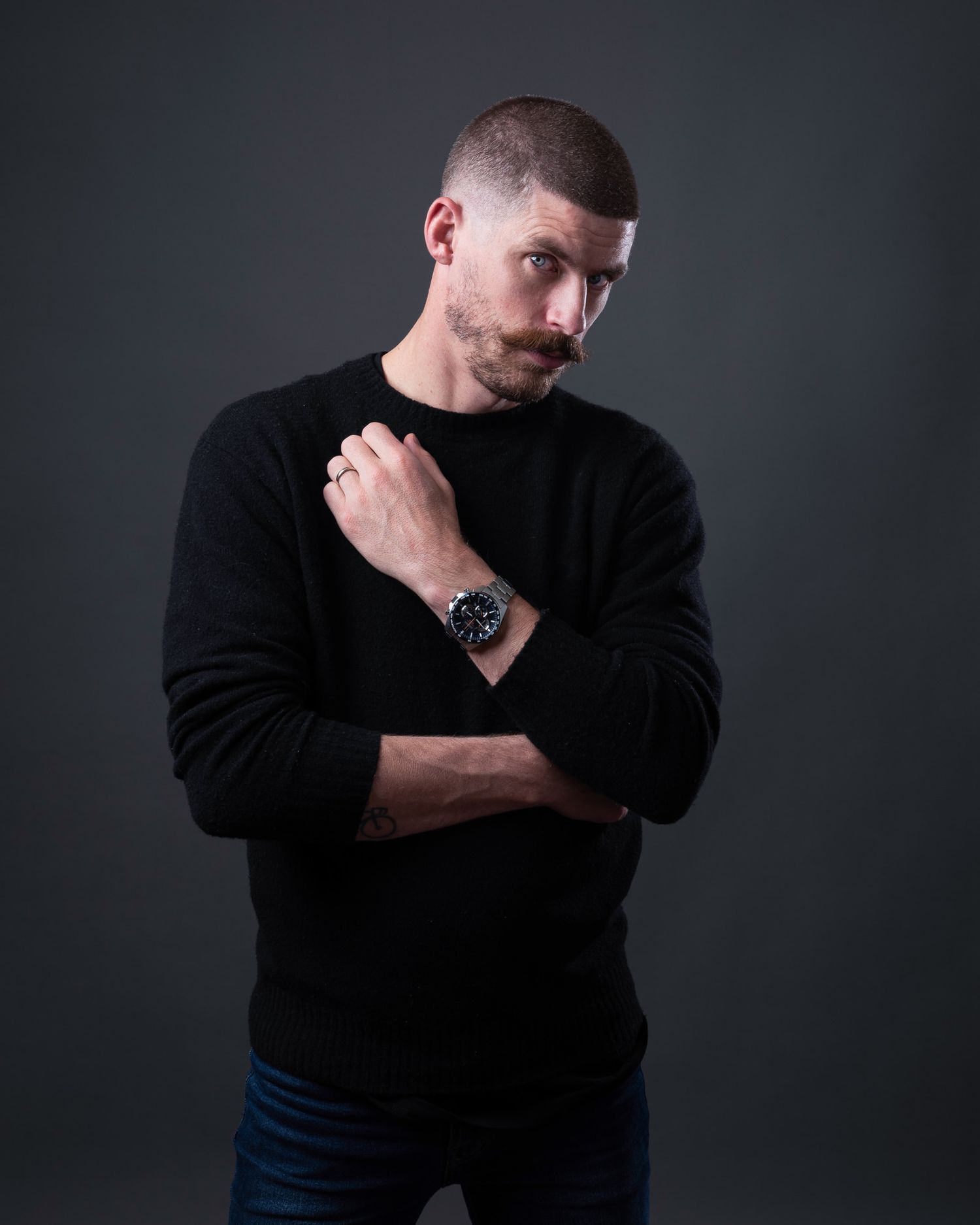 Stylish portrait of a person in a black sweater showing off a luxury watch against grey backdrop.