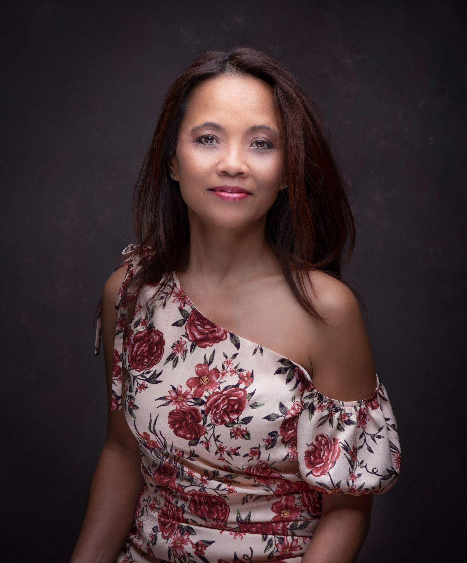 Studio portrait showing a model wearing an elegant floral one-shoulder dress in red and white against a dark background.