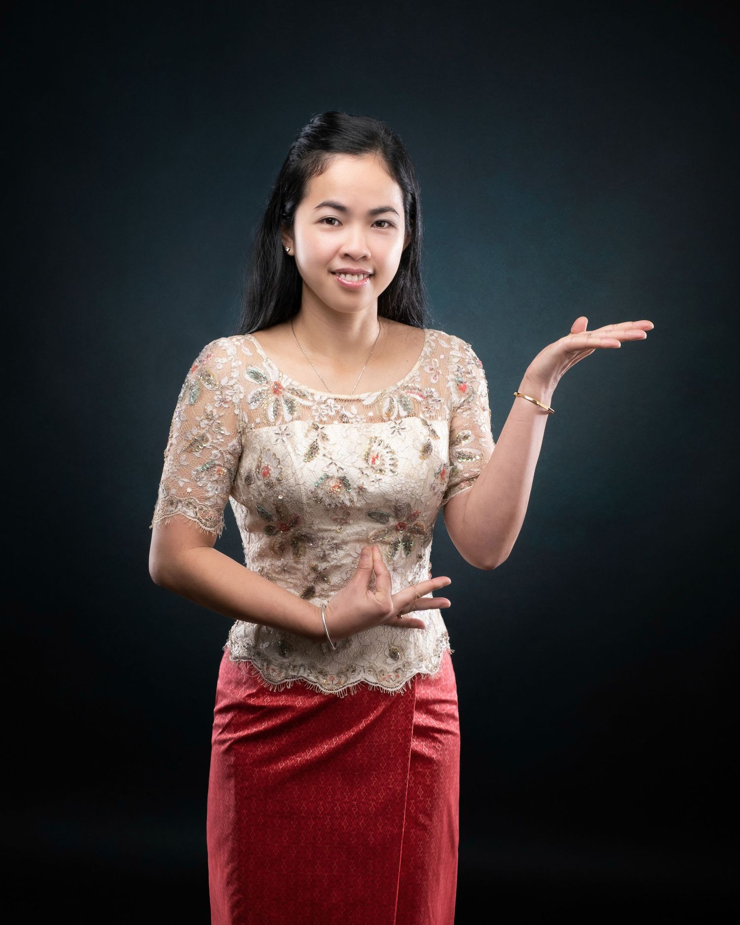 Person in a beige lace top and red skirt poses elegantly against a dark background with an expressive hand gesture.