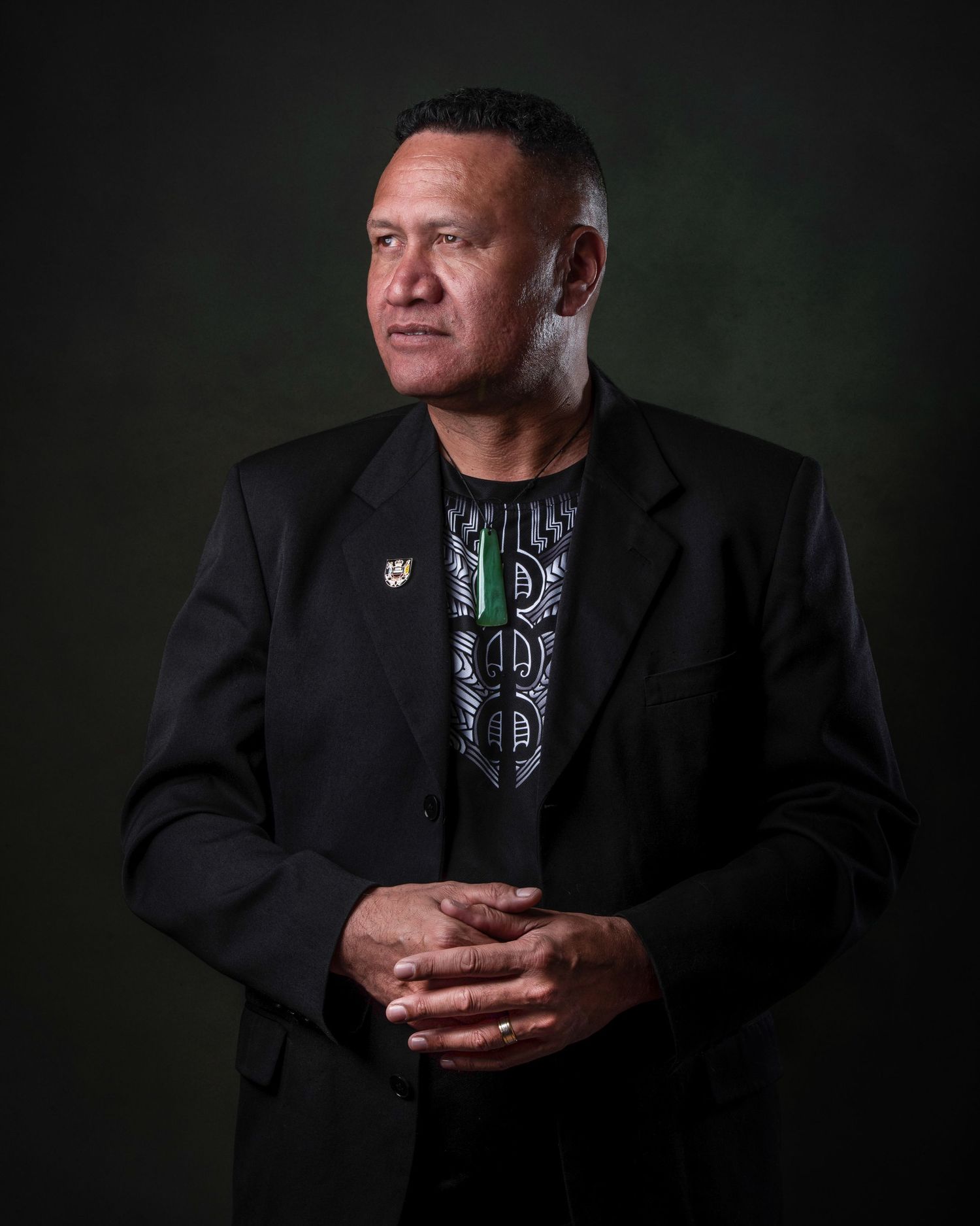 Portrait photograph of person in black blazer and graphic t-shirt against dark green backdrop.