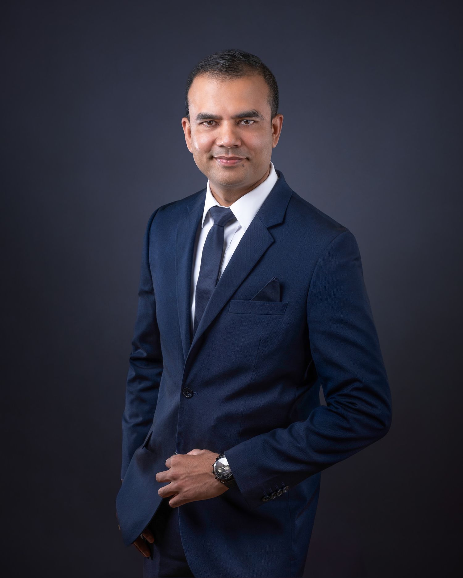 Professional headshot of person in navy suit and tie against dark background.