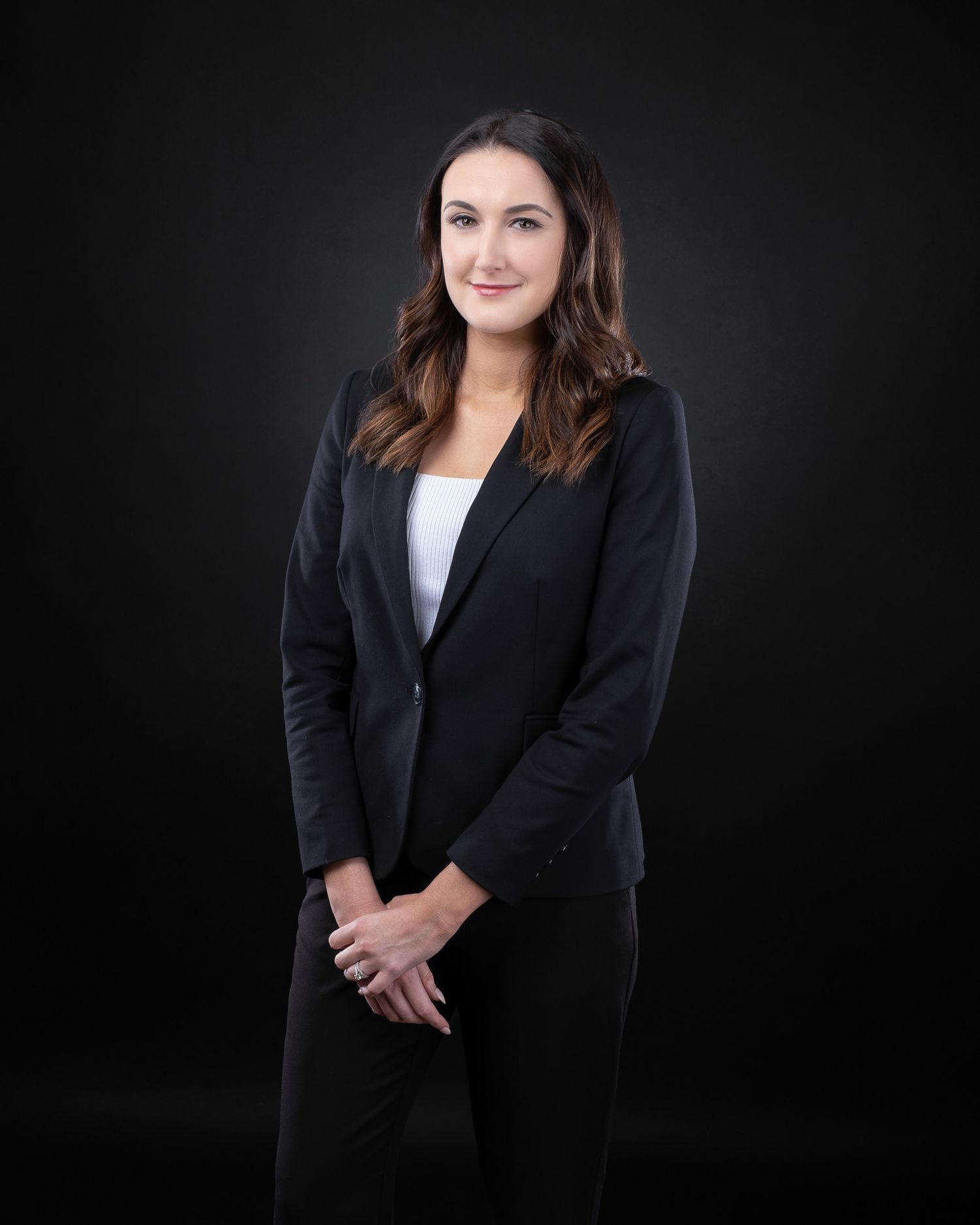 Professional headshot of person in black blazer and white top against dark backdrop.
