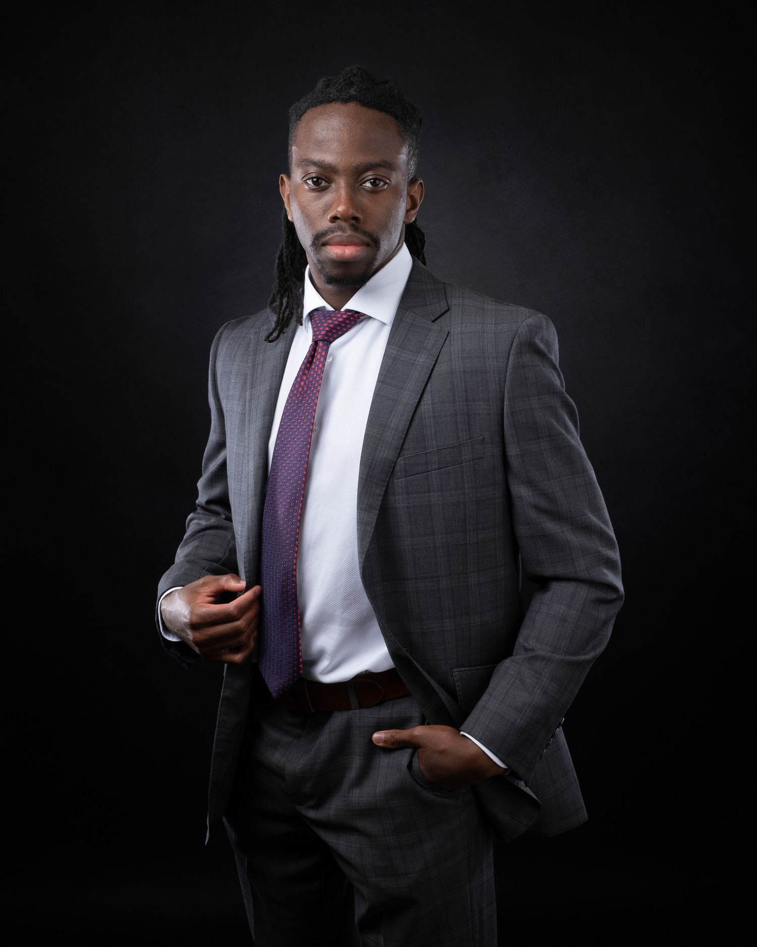 Professional business portrait of person in dark suit and purple tie holding phone against black background.