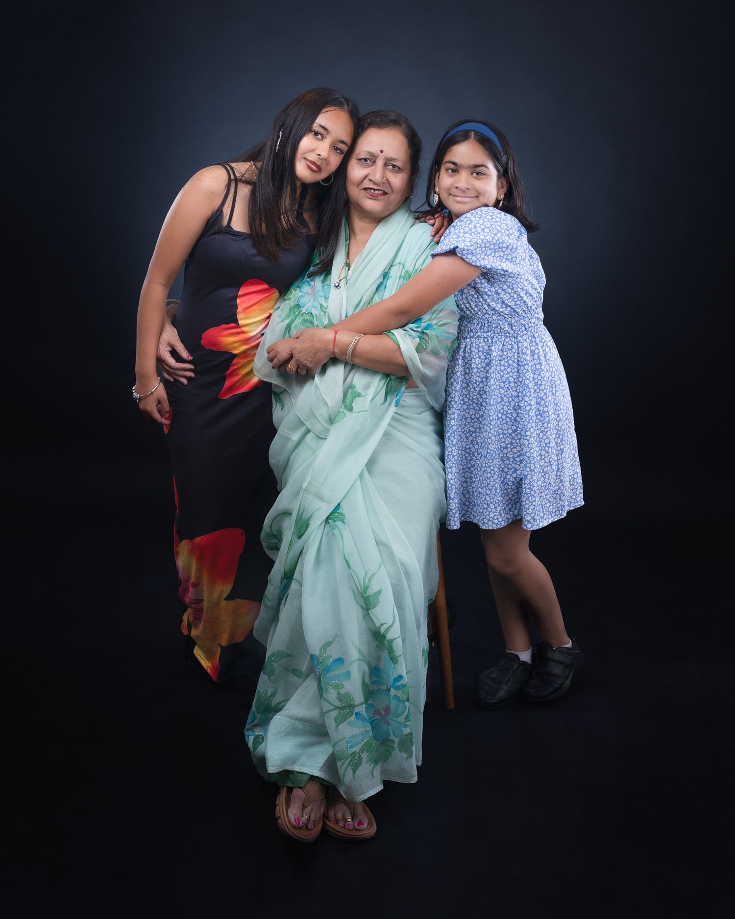 Studio portrait of three generations in coordinated outfits against a dark background.