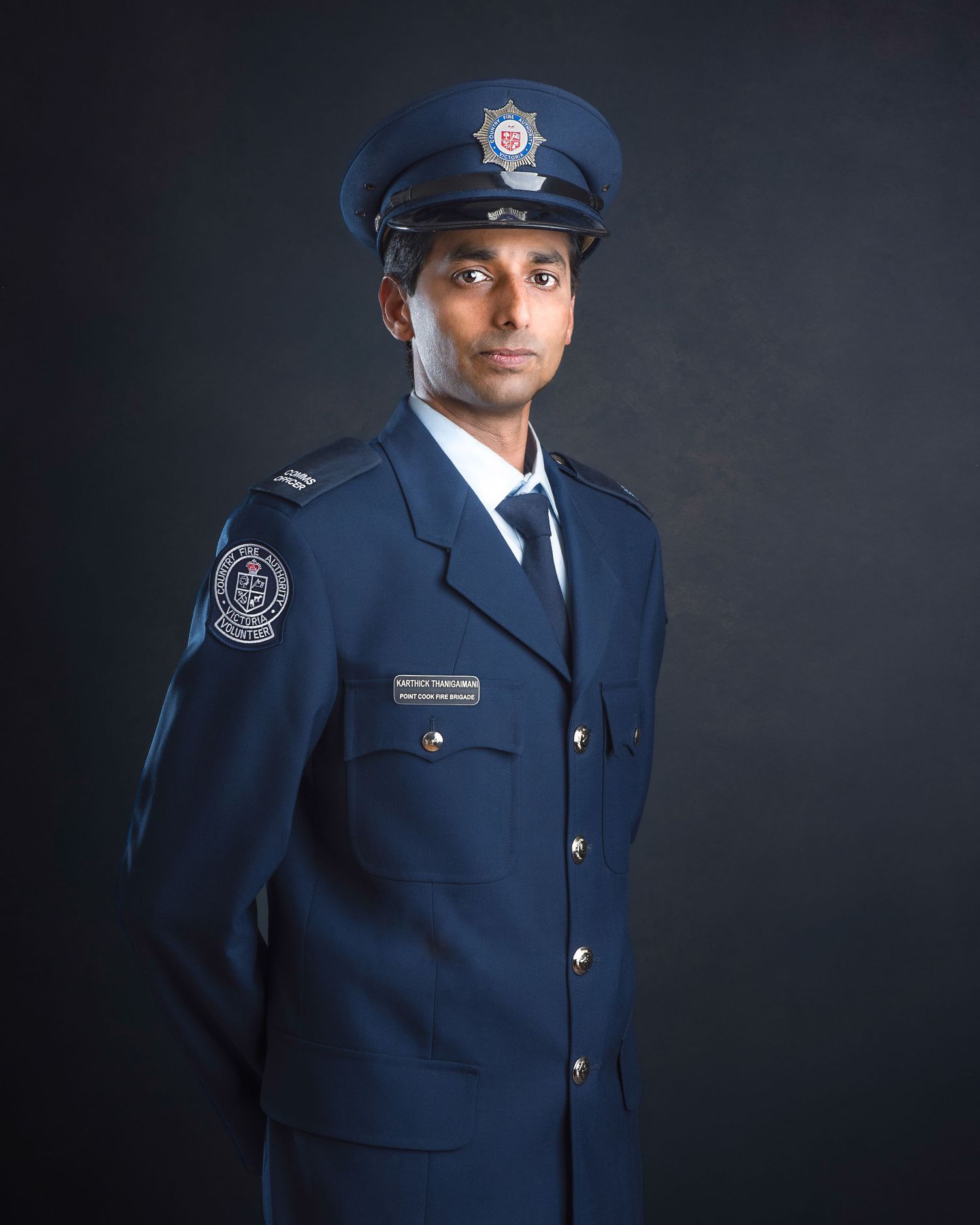 Professional studio portrait of a uniformed police officer in a navy blue dress uniform and cap against dark background.