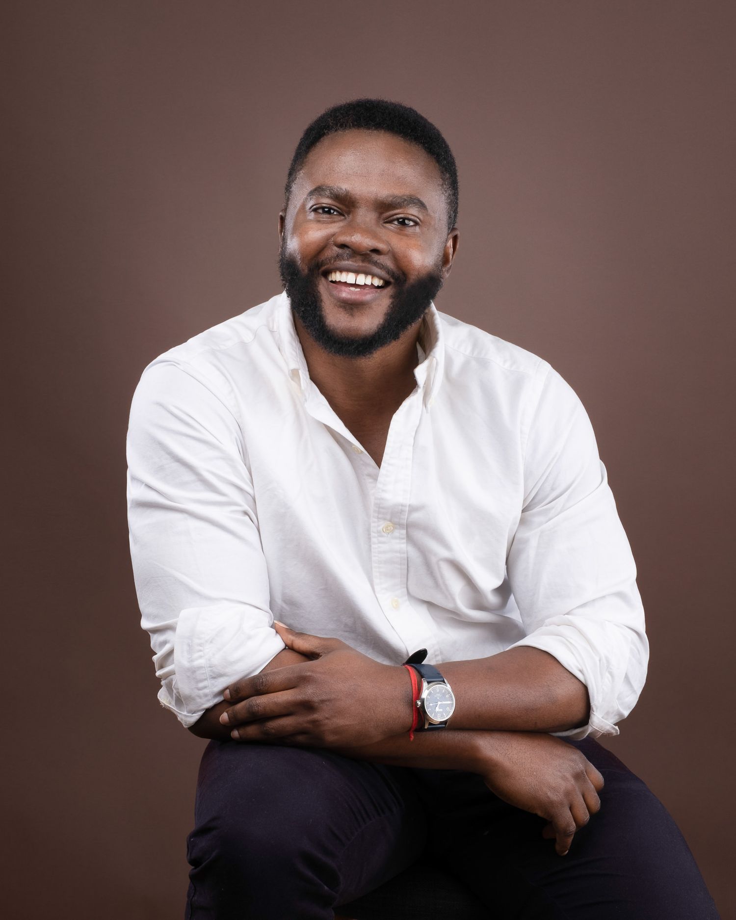 Professional studio portrait of someone in a crisp white button-down shirt against brown background, wearing a watch.