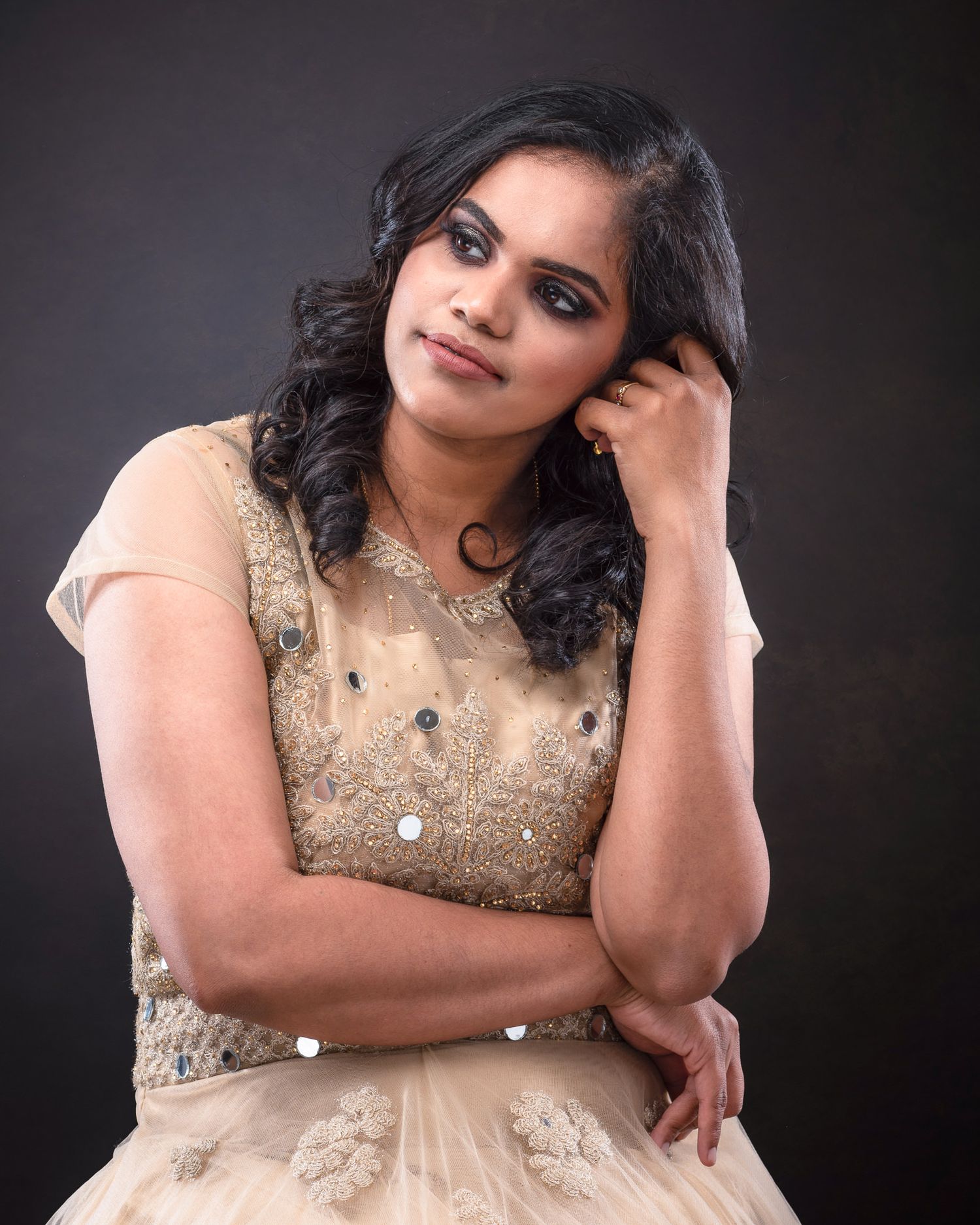 Portrait of a person in a glittering beige dress with intricate embellishments posing against a dark background.