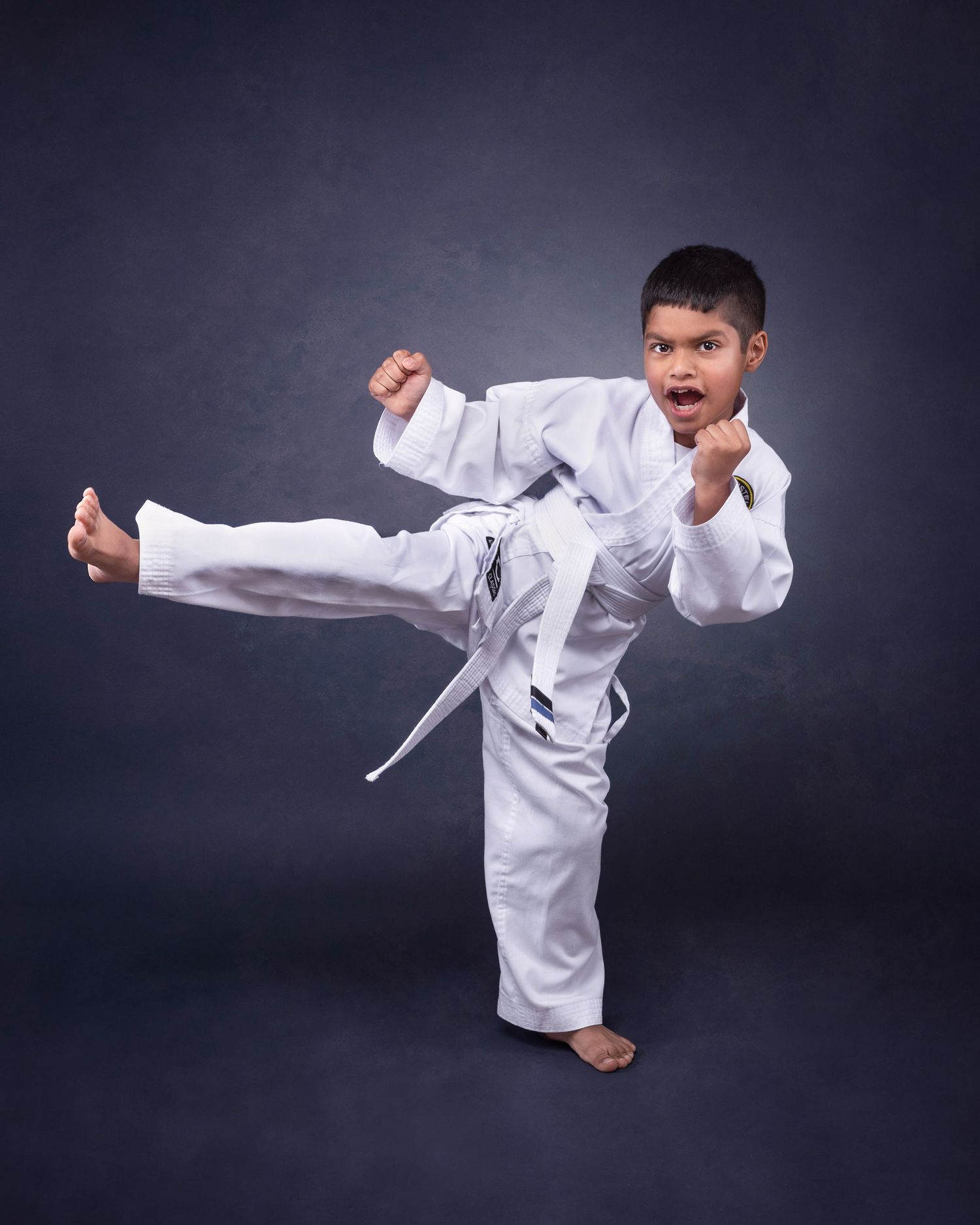 A martial artist in a white karate gi performs a dramatic side kick against a dark studio background.
