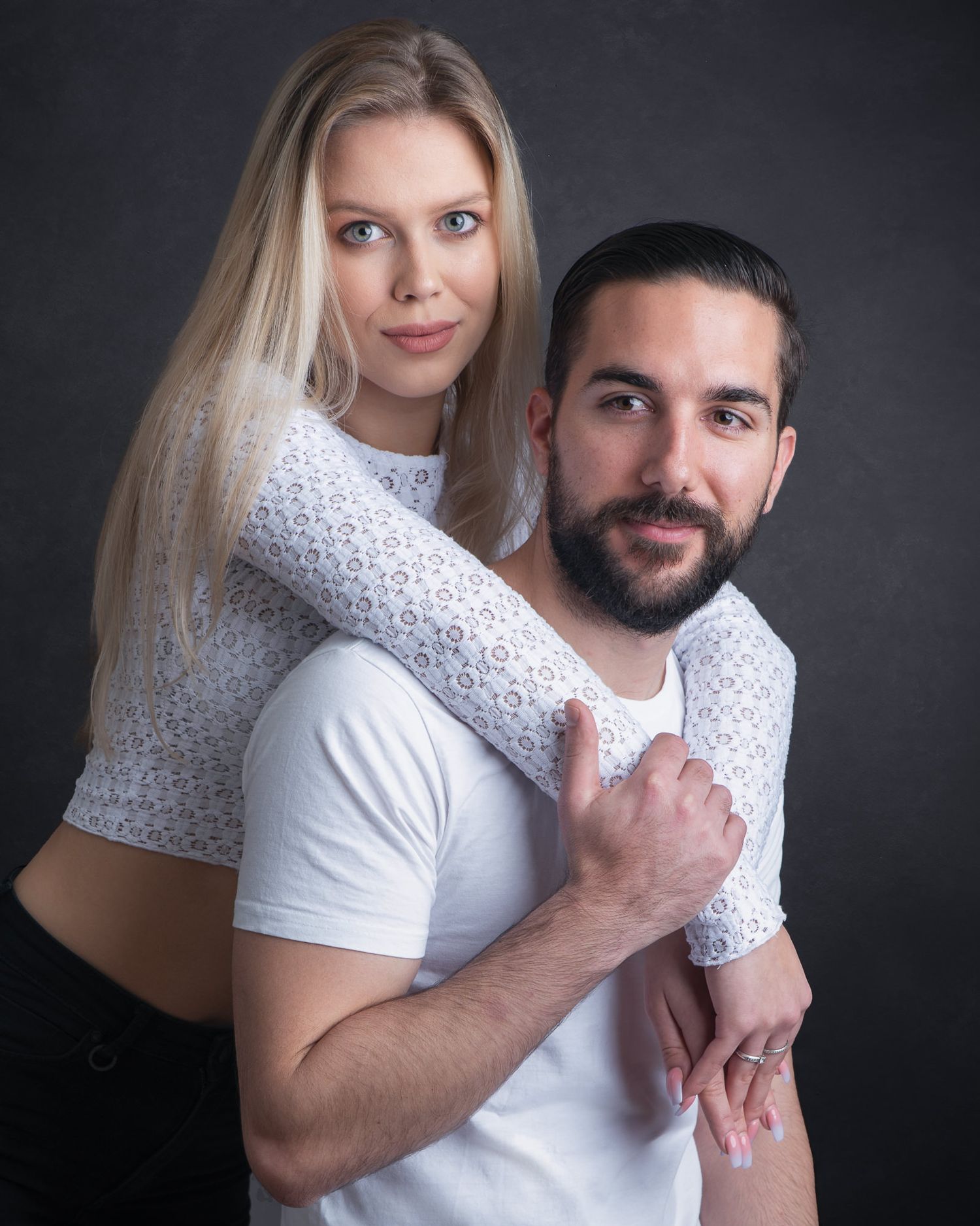 Studio portrait of two people posing together against dark background in white clothing with artistic lighting.