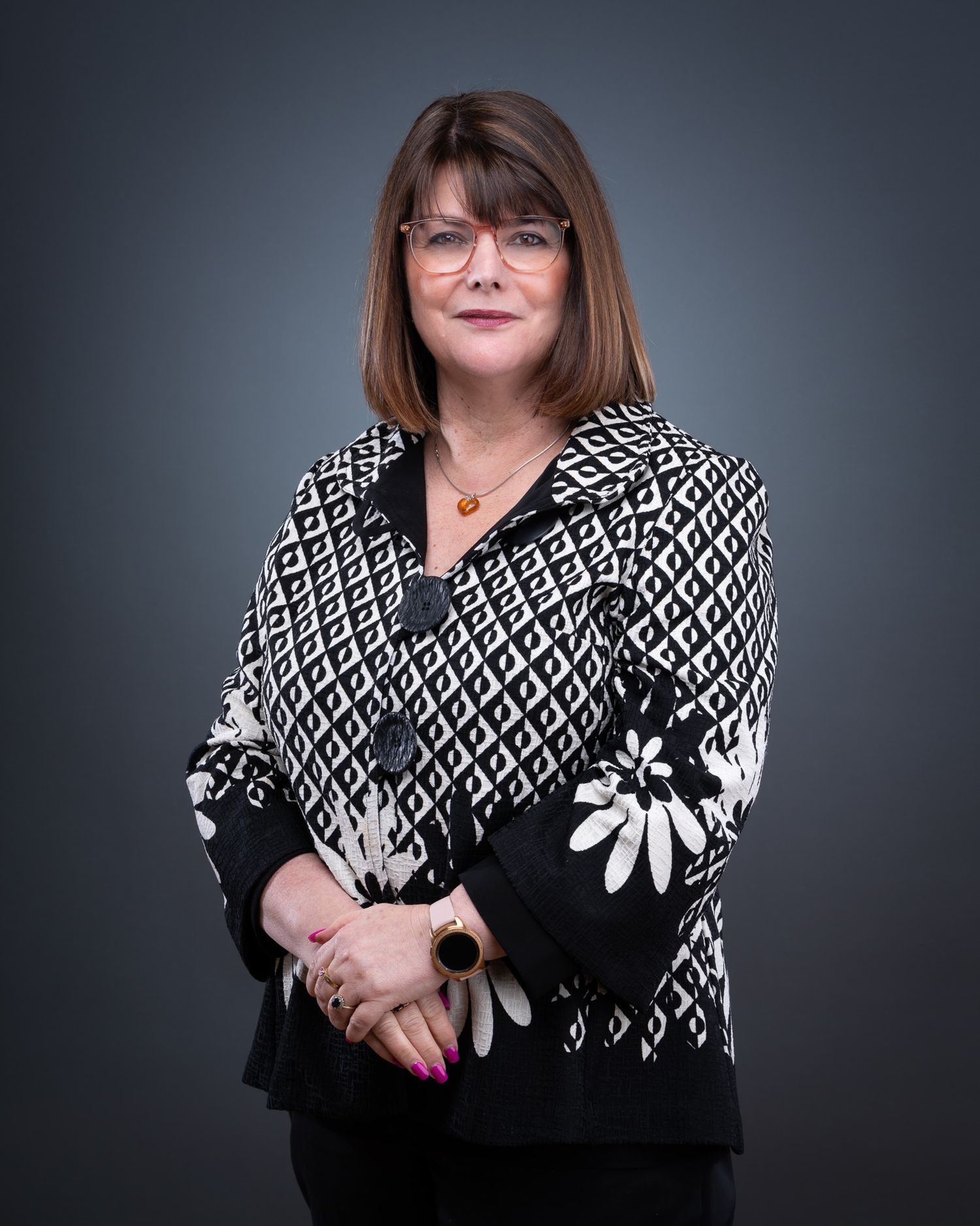 Professional studio portrait of person wearing black and white patterned sweater with floral design against dark background.