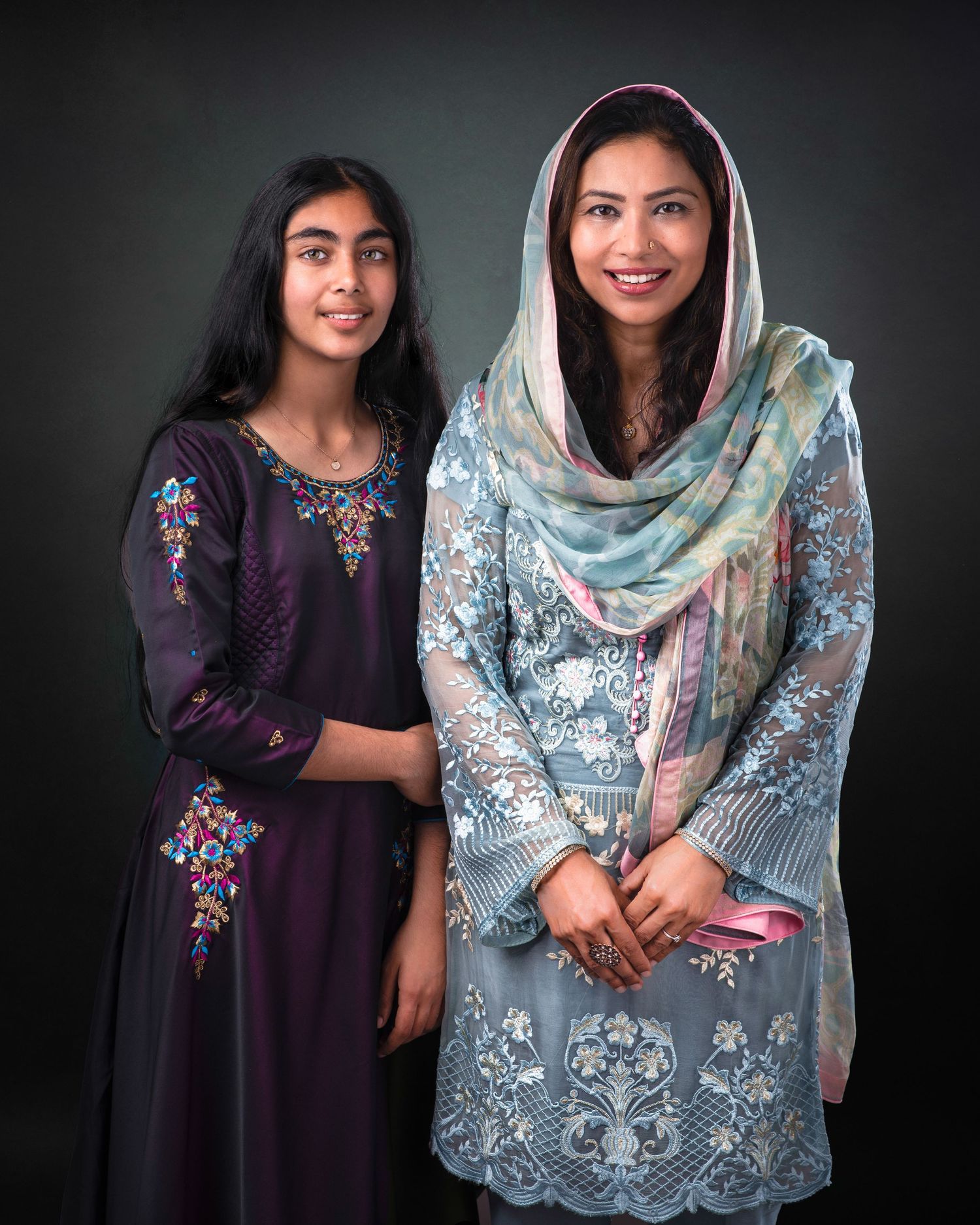 Two people in traditional South Asian attire pose together against a dark background for a portrait.