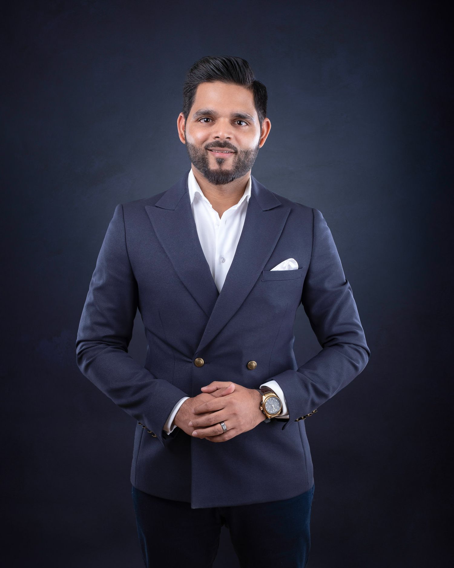 Professional studio portrait of someone in a navy double-breasted blazer and white dress shirt against dark background.