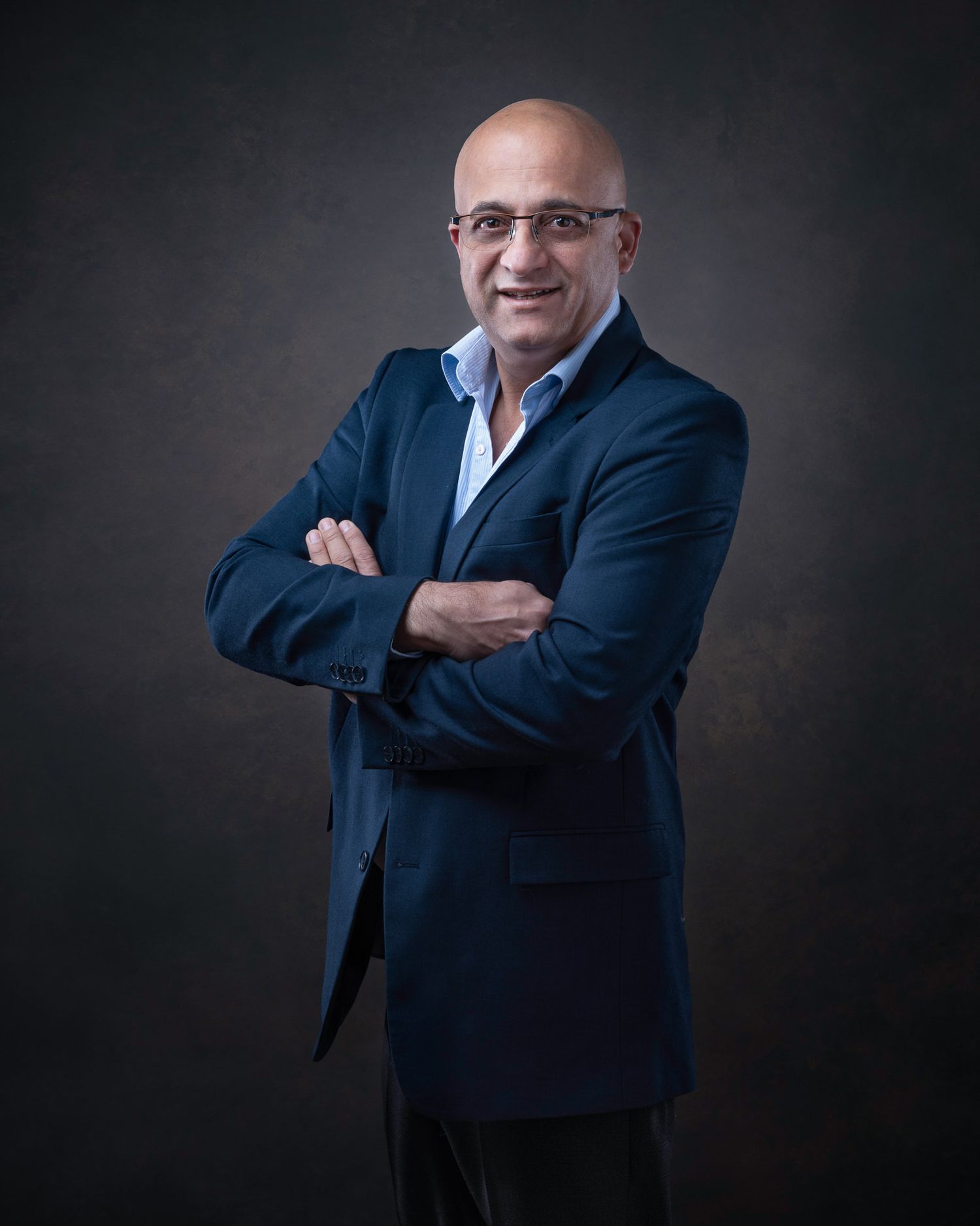 Professional studio portrait of a businessman in a navy blazer and light blue shirt with arms crossed.