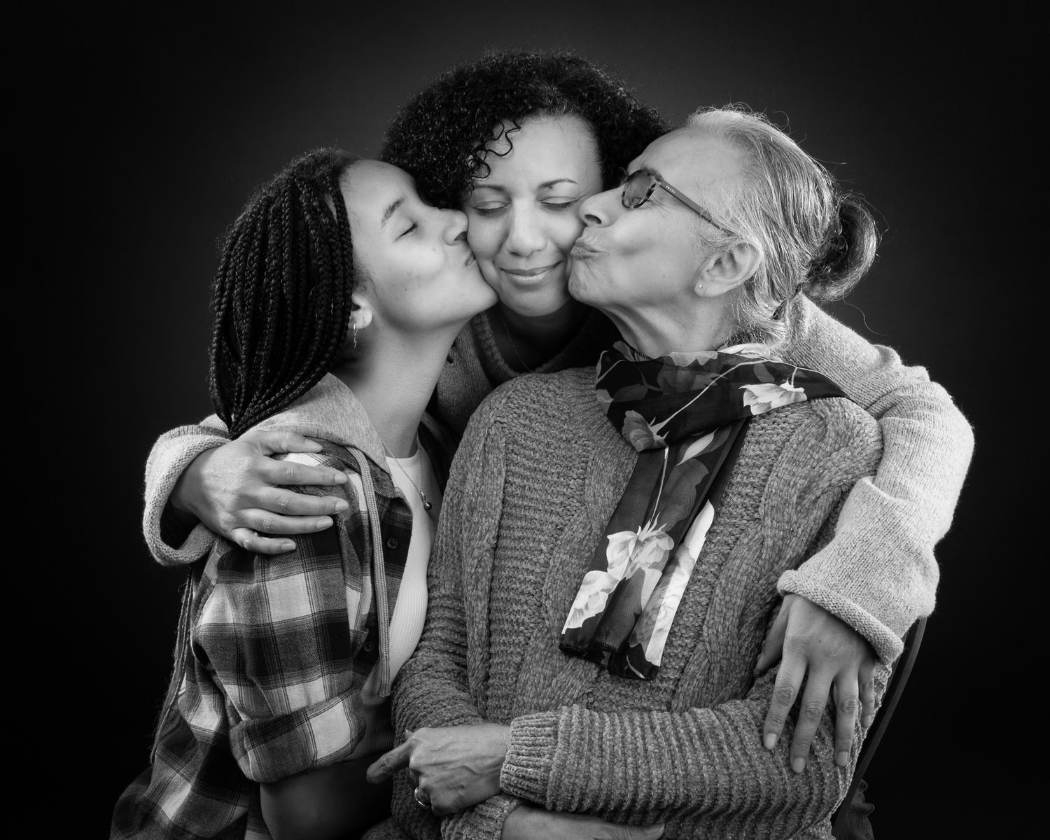 A heartwarming black and white portrait of three generations sharing kisses and embraces together.