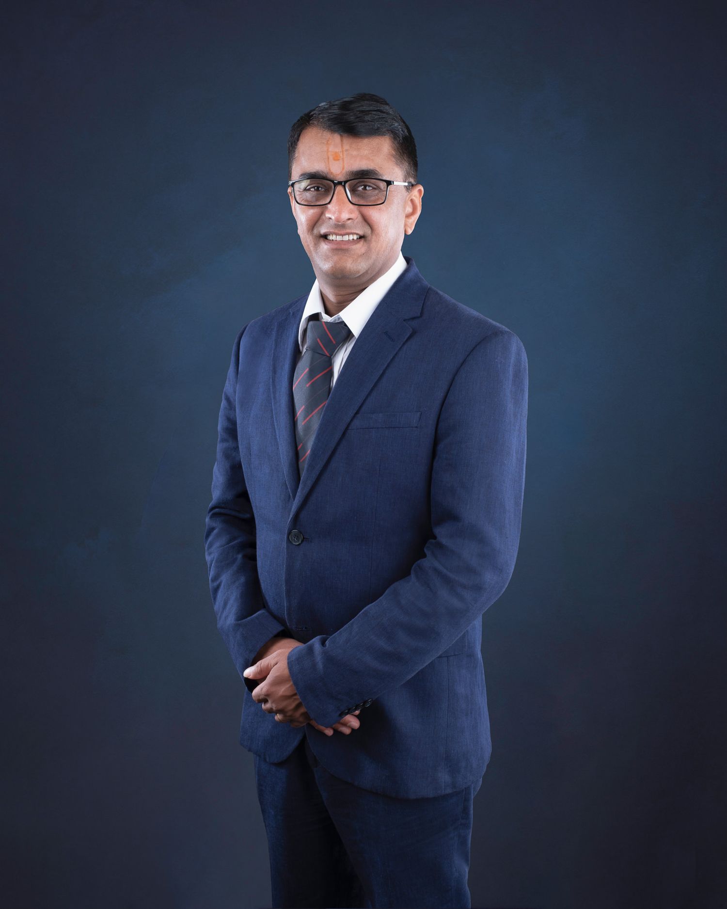 Professional business portrait of person in navy suit and tie against dark background.