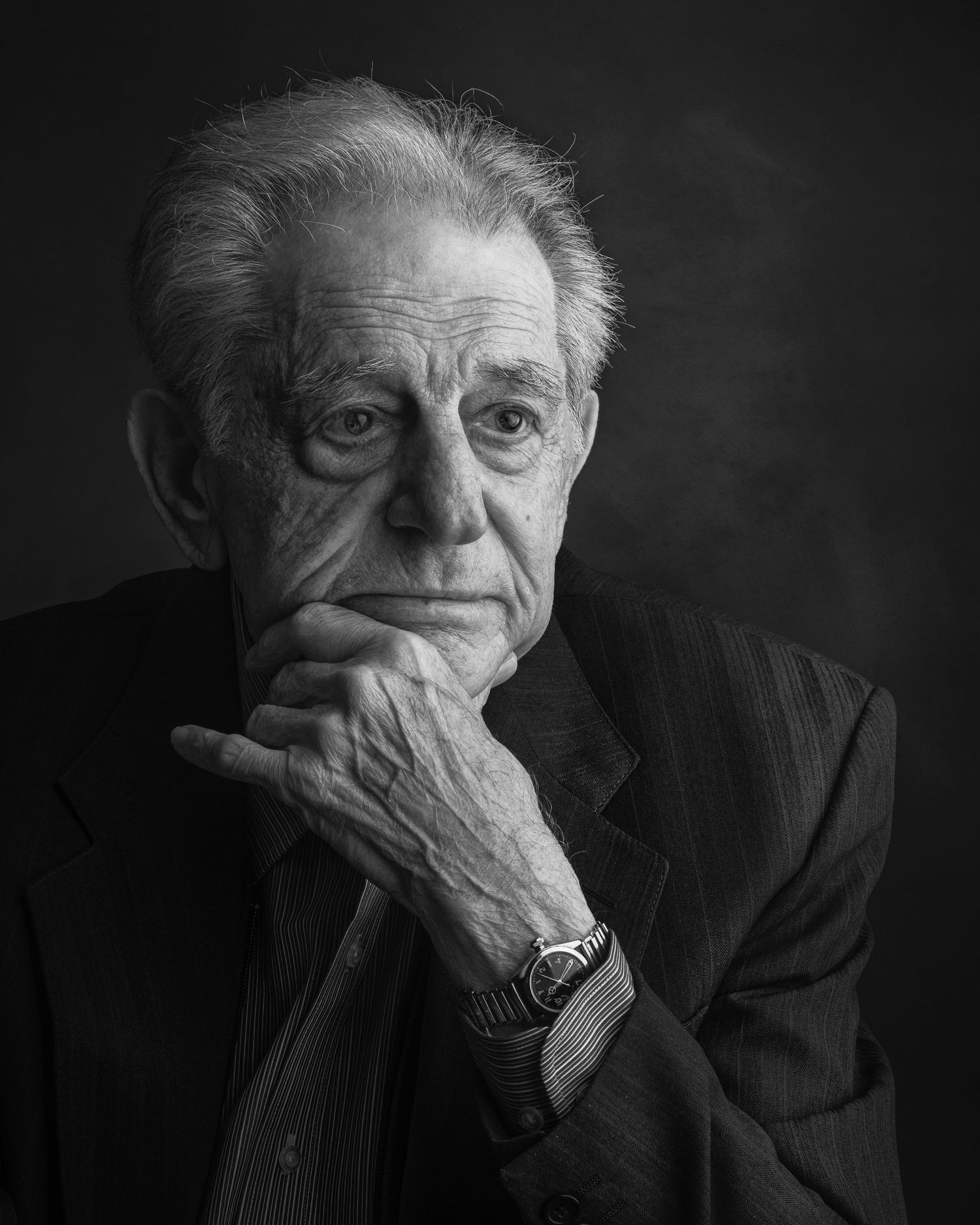 Black and white portrait of an elderly person in formal attire with hand resting on chin in contemplative pose.