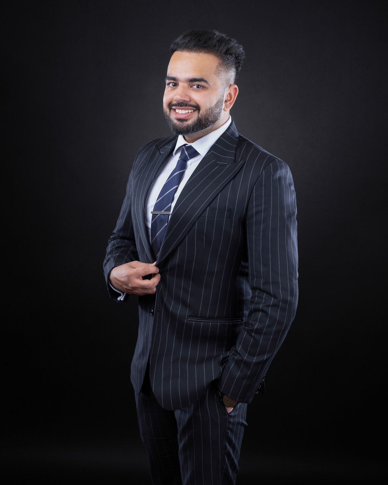 Professional portrait of a smiling businessman in a pinstriped suit and blue tie against a dark background.