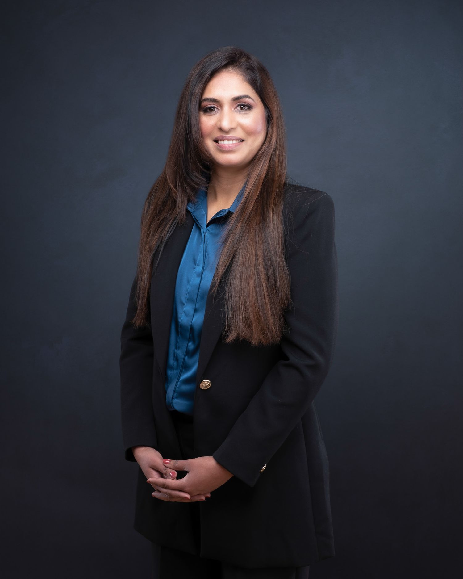 Professional studio portrait in formal business attire with black blazer and blue blouse against dark background.