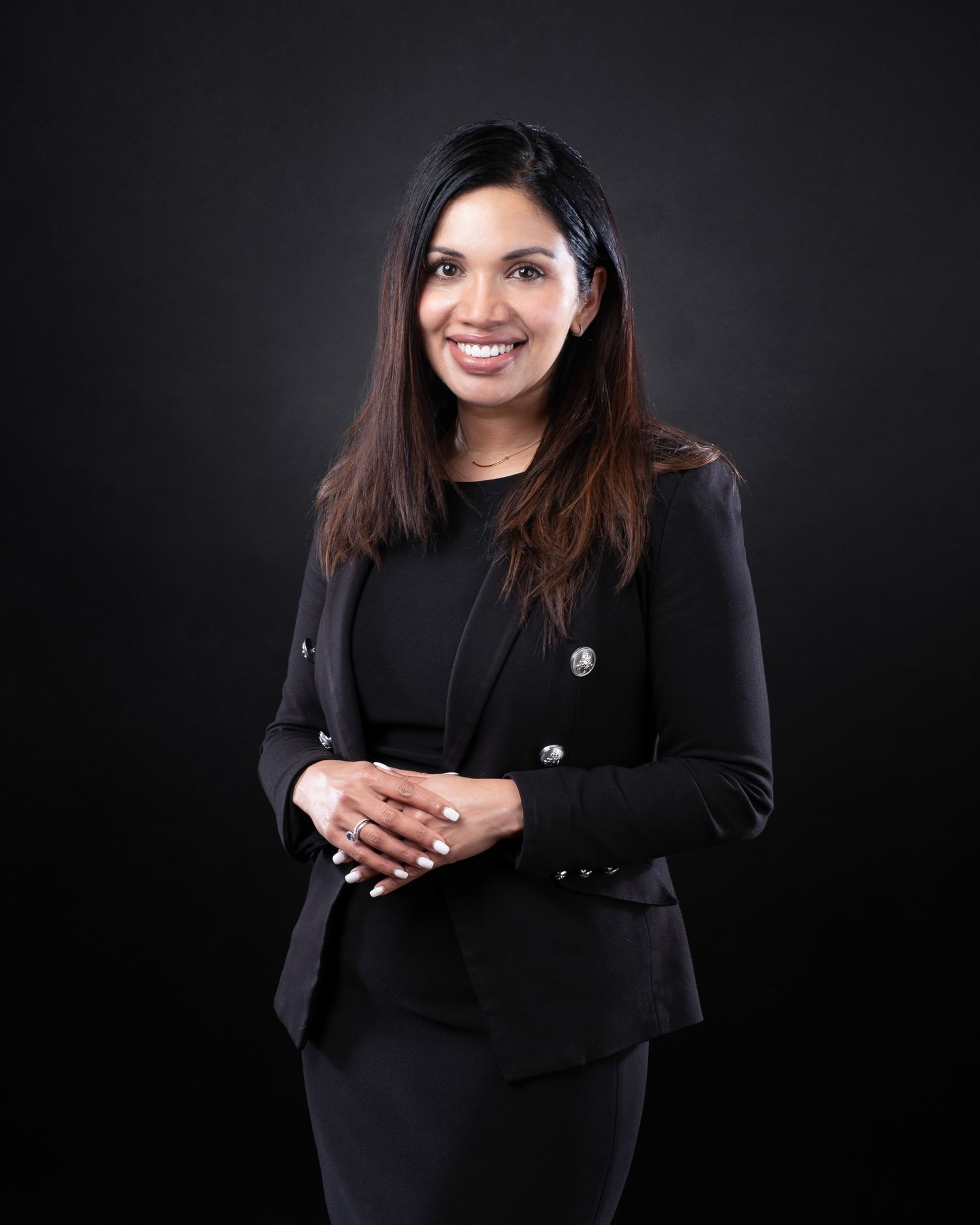 Professional headshot of a businesswoman wearing a black suit against a dark studio background.