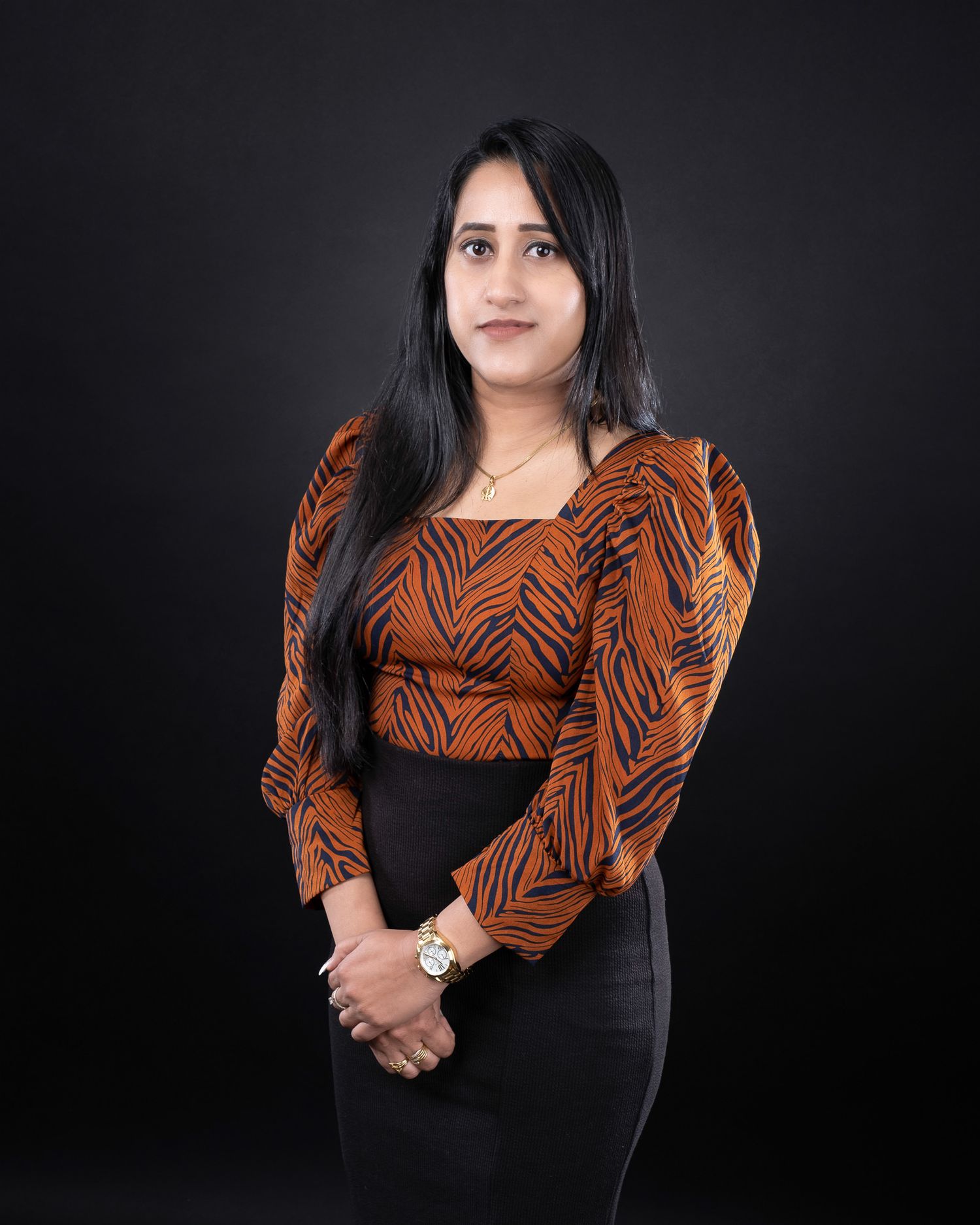 Studio portrait of a person in a brown patterned top and black outfit against a dark background.