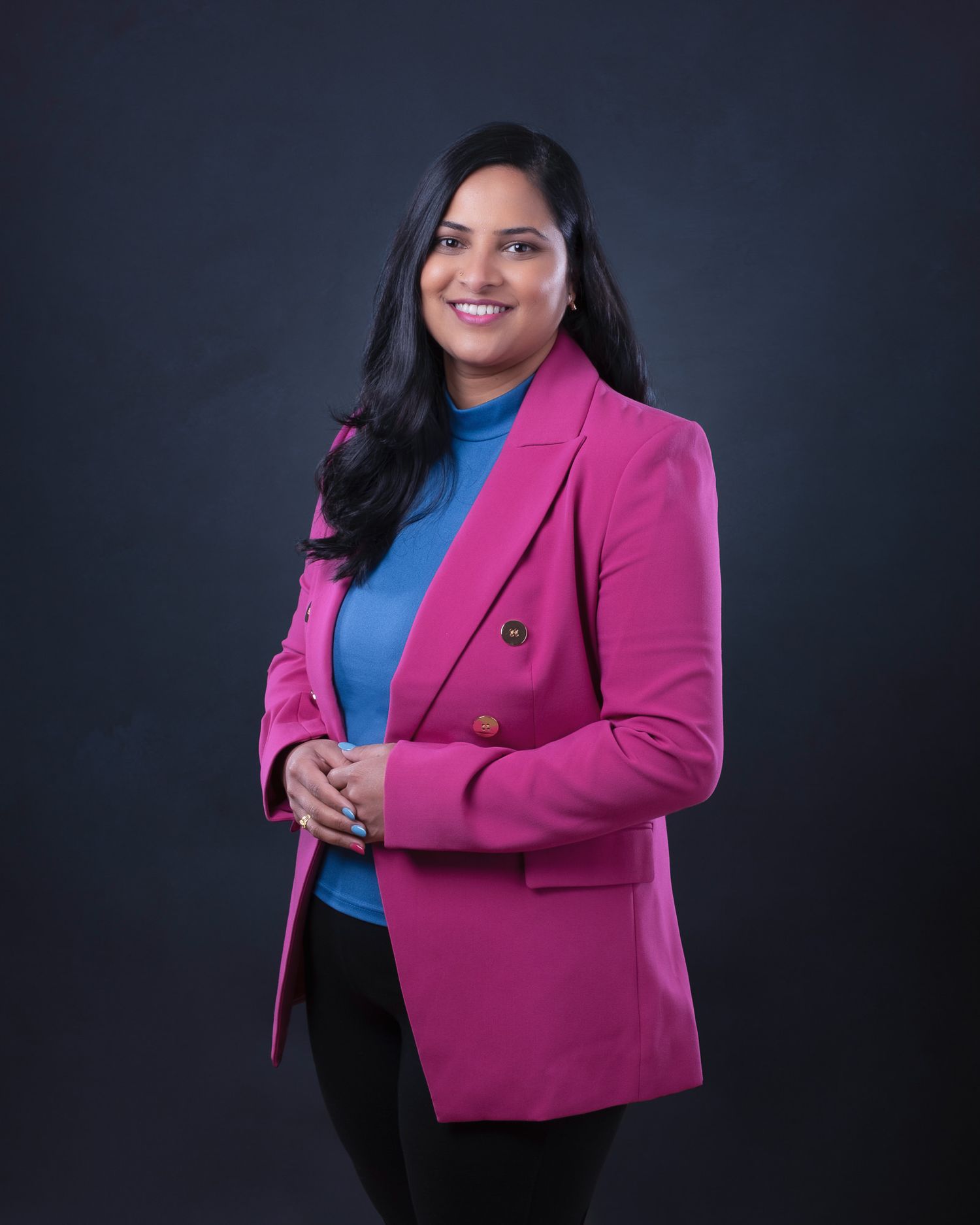 Professional portrait of someone in a vibrant pink blazer and blue top against a dark background.