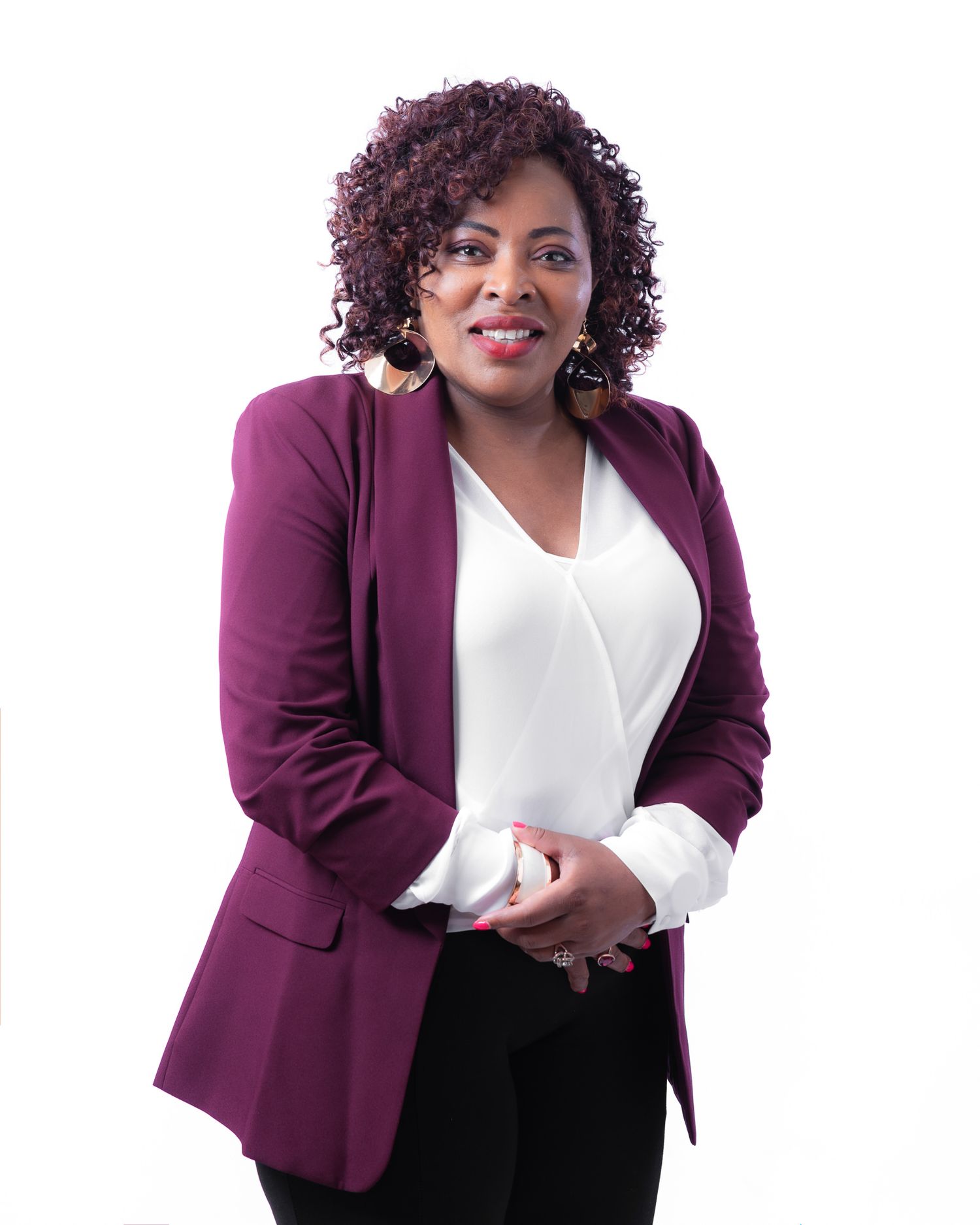 Professional wearing a burgundy blazer and white blouse stands against white background in business attire.