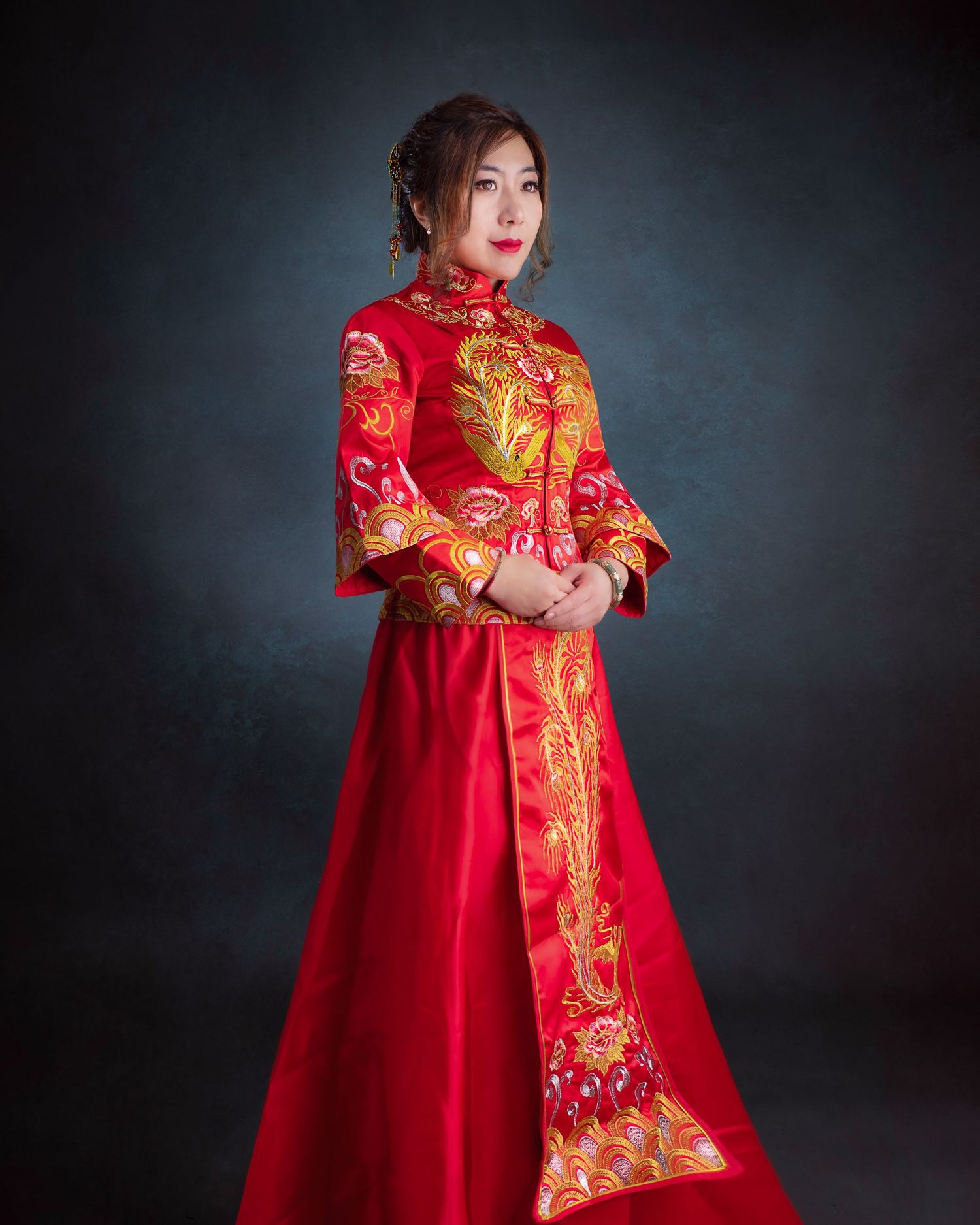 Traditional Chinese wedding dress in bright red with intricate gold embroidery photographed against dark backdrop.