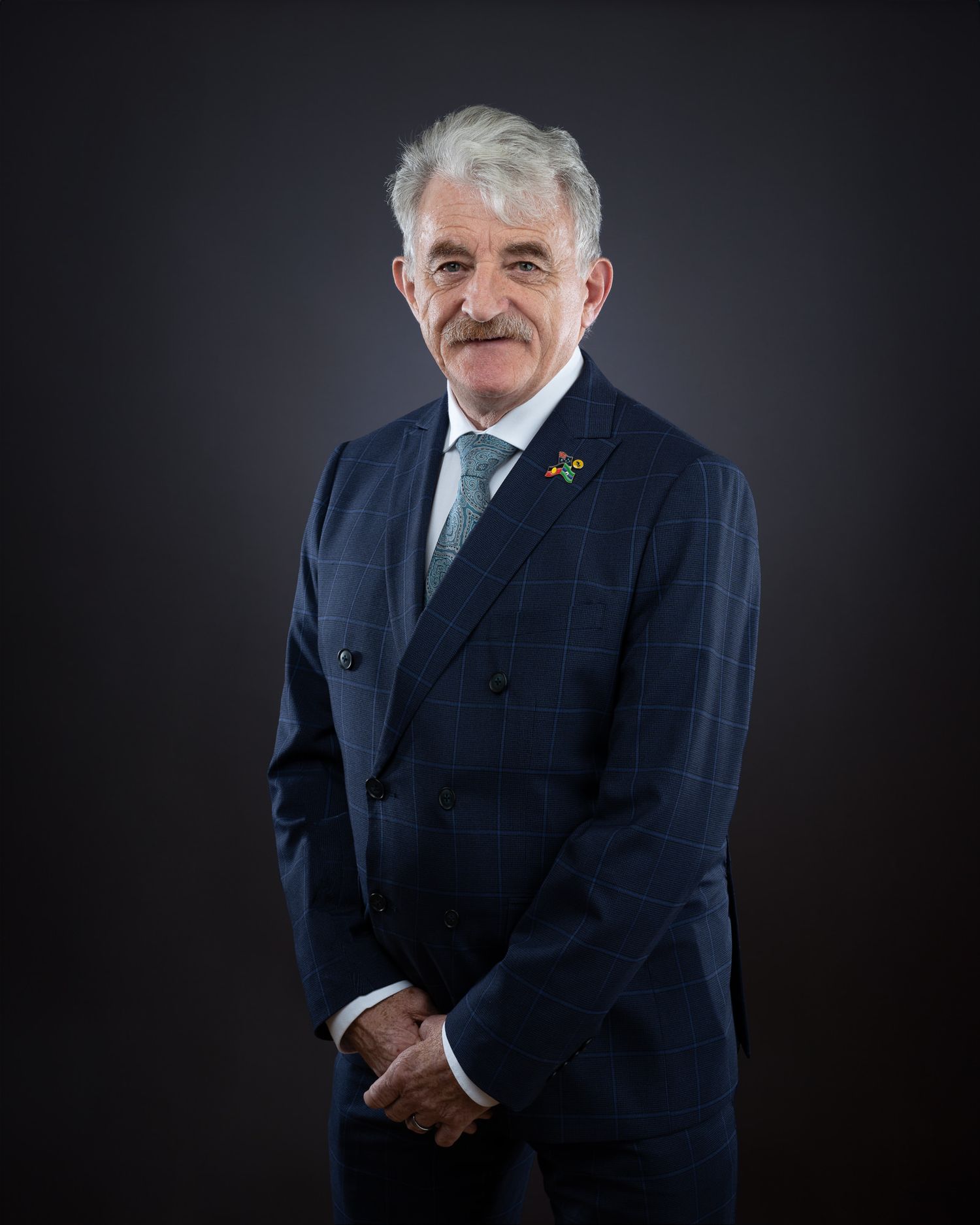 Professional portrait of person in navy suit with green tie against dark background.