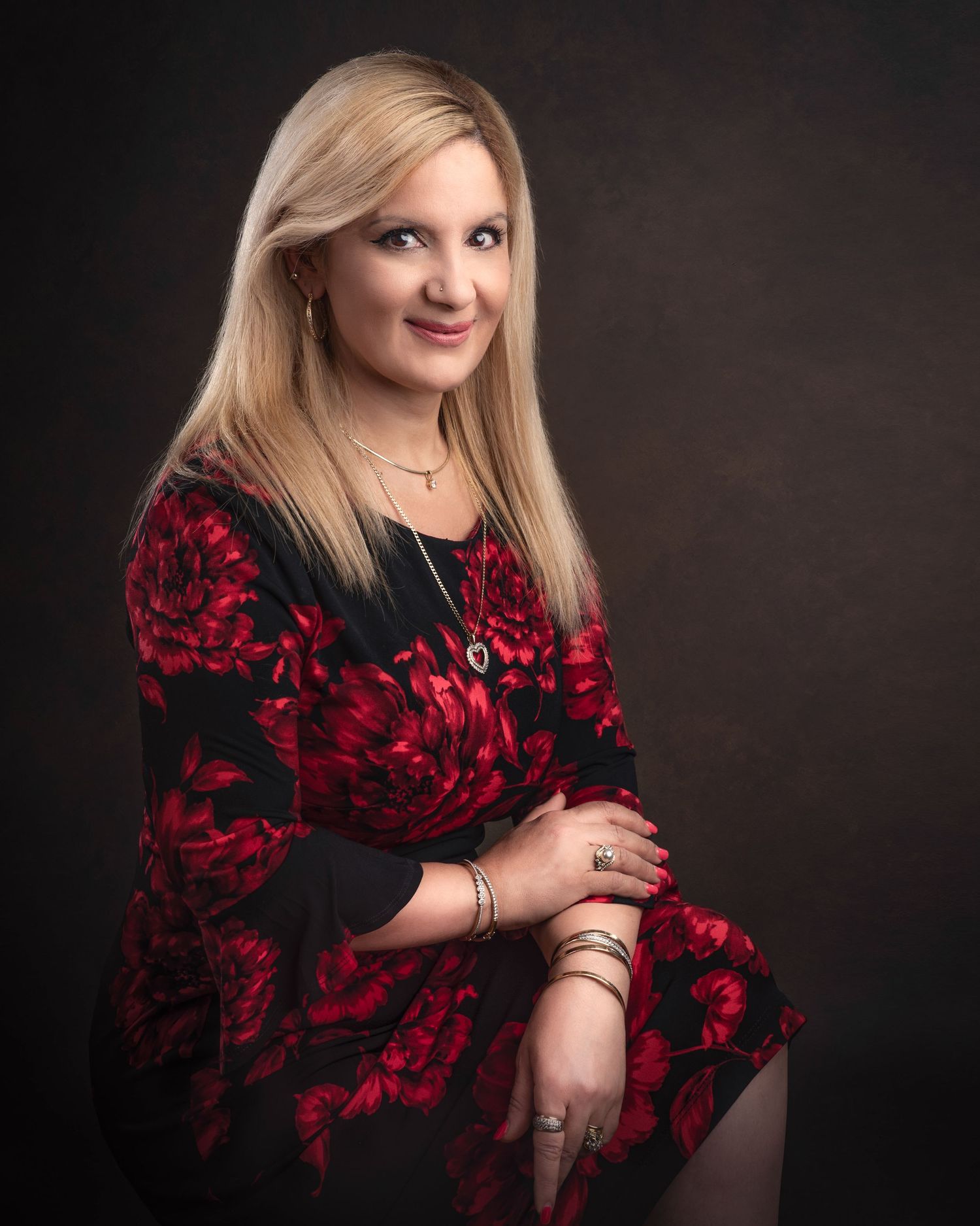 Professional studio portrait of someone wearing a black and red floral dress against a dark background.