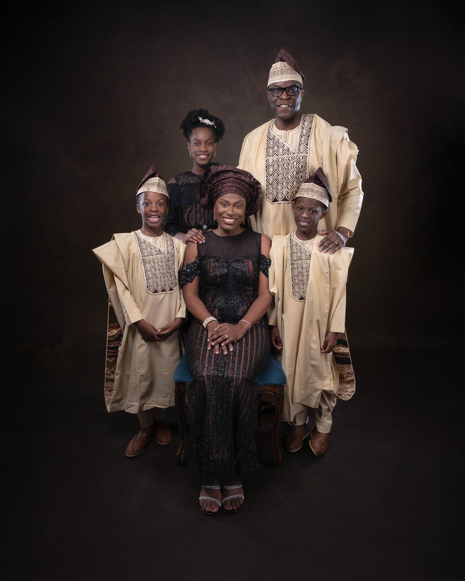 Portrait of a family in traditional African clothing with yellow agbada robes and formal attire against dark background.