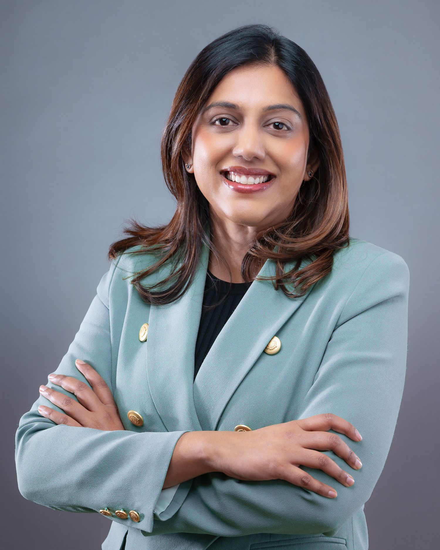 Professional portrait of someone in a mint green blazer with gold buttons smiling against a grey background.