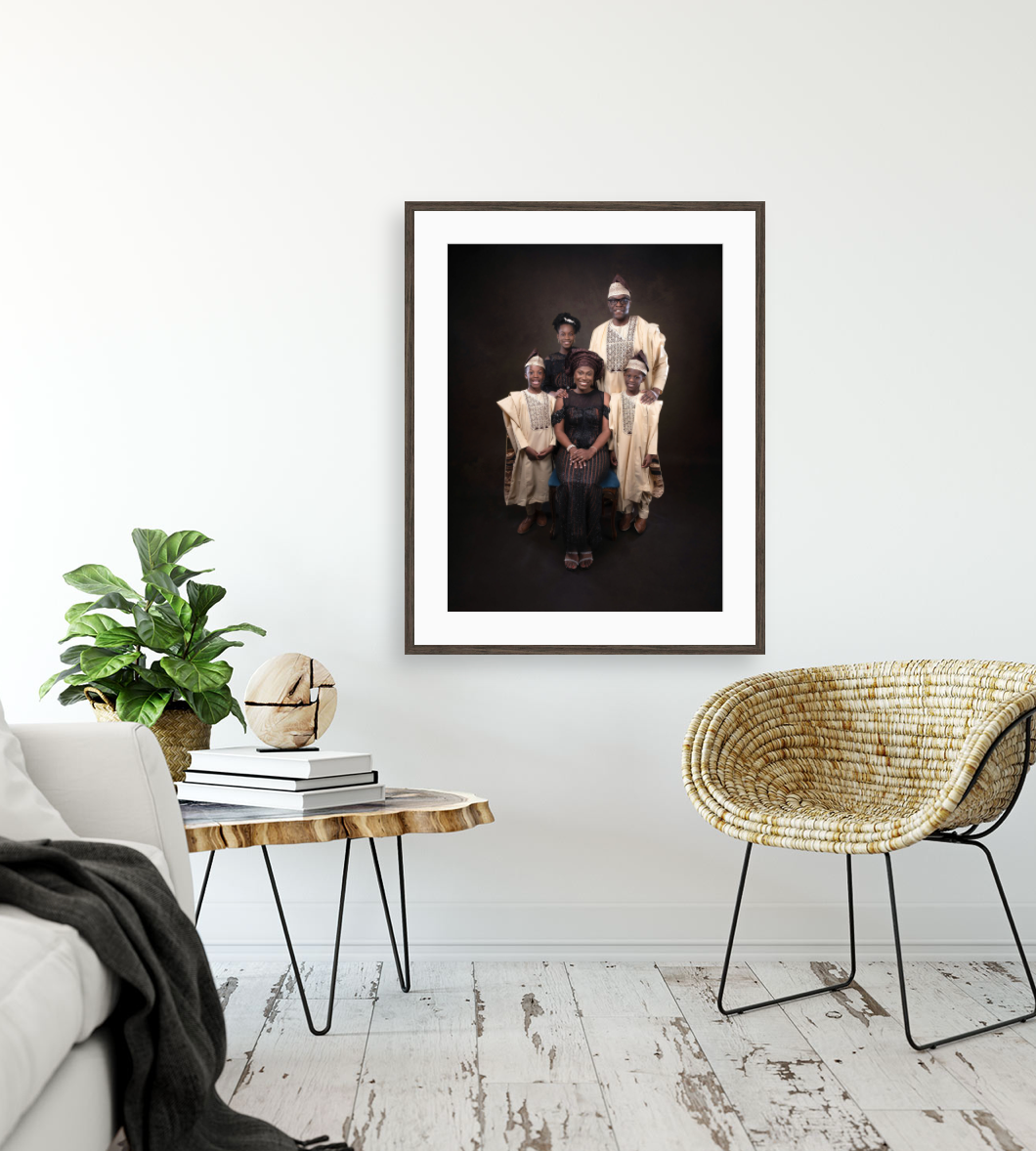 A framed black and white portrait photograph displayed in a modern living room with white floors and wicker chair.