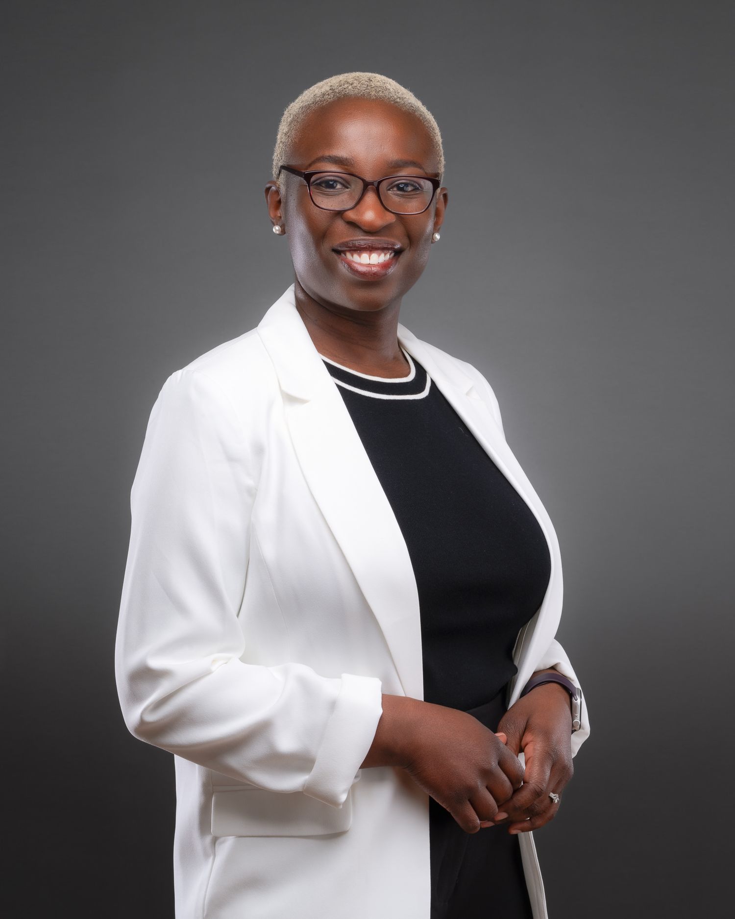 Professional business portrait of person in white blazer and black top smiling against dark gray background.