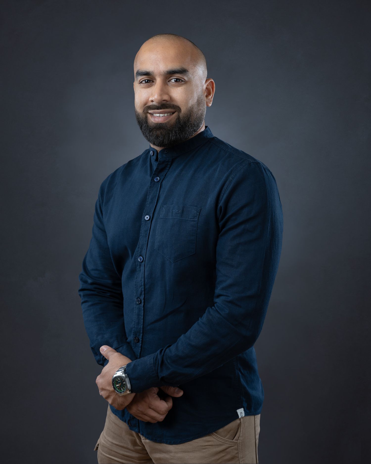 Professional studio portrait of person in navy button-down shirt against dark background with soft lighting.
