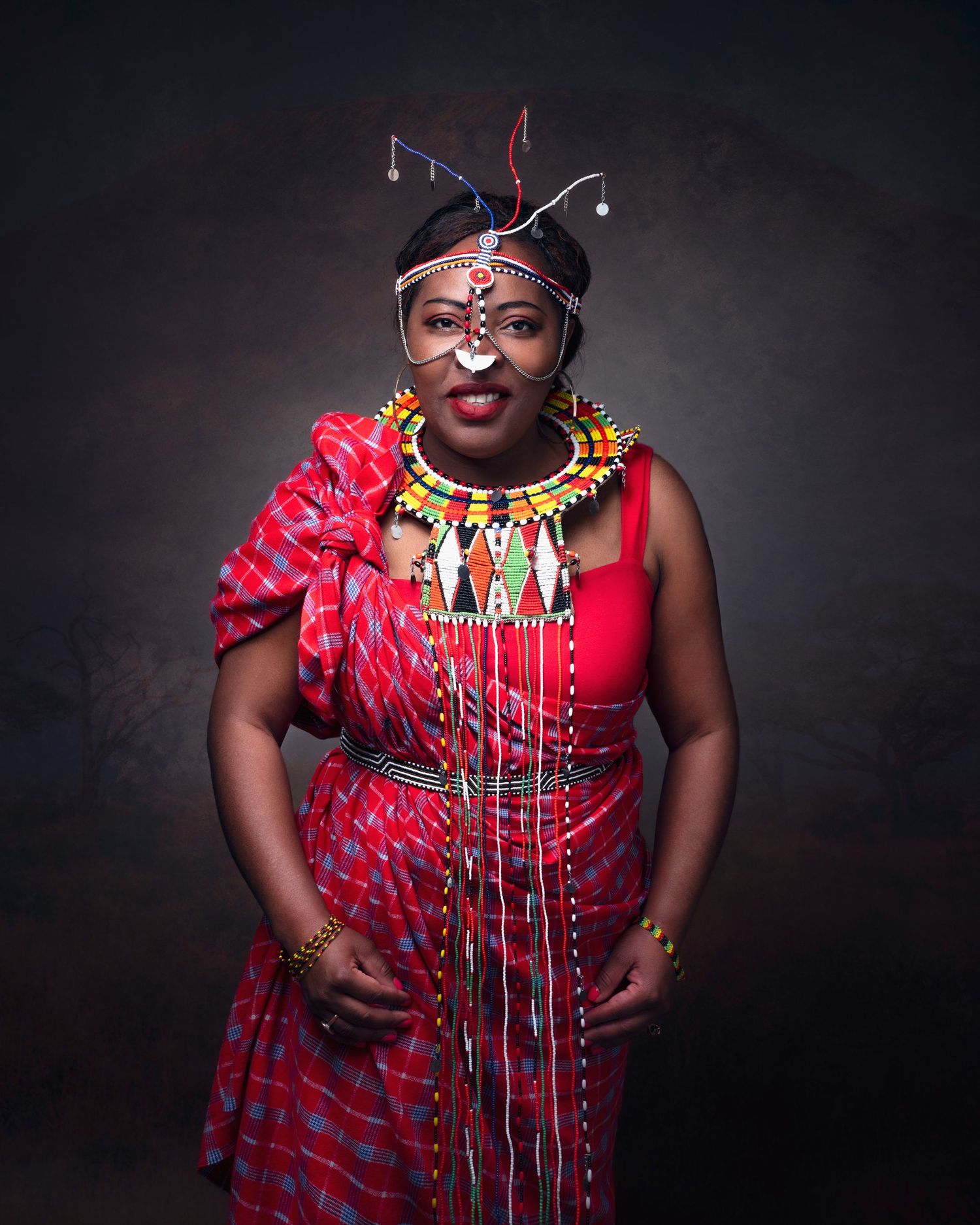 A person wearing traditional African attire including a red patterned dress, ornate necklace and decorative headpiece against dark backdrop.