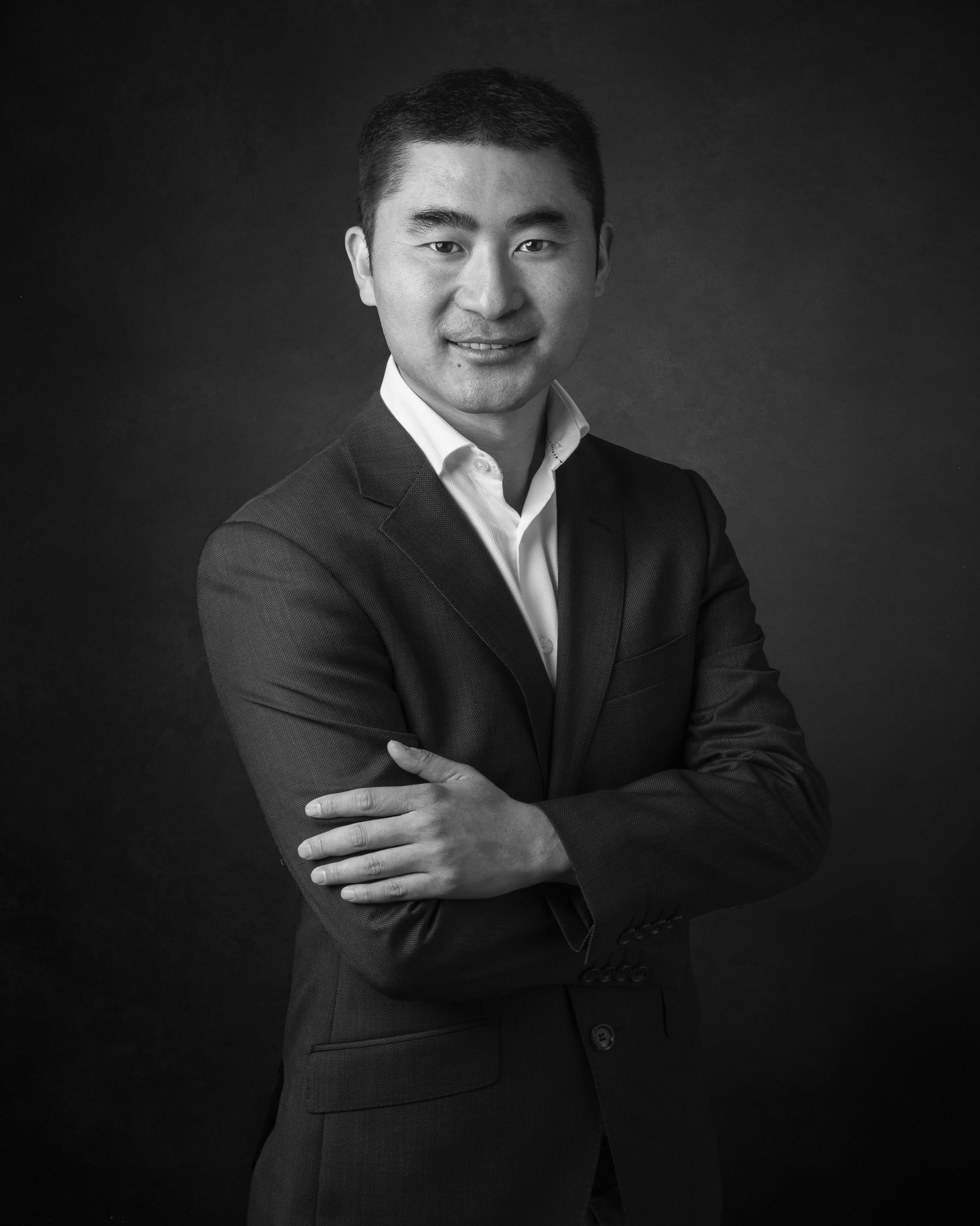 Professional black and white portrait of a person in a dark suit jacket and white dress shirt against a dark background.