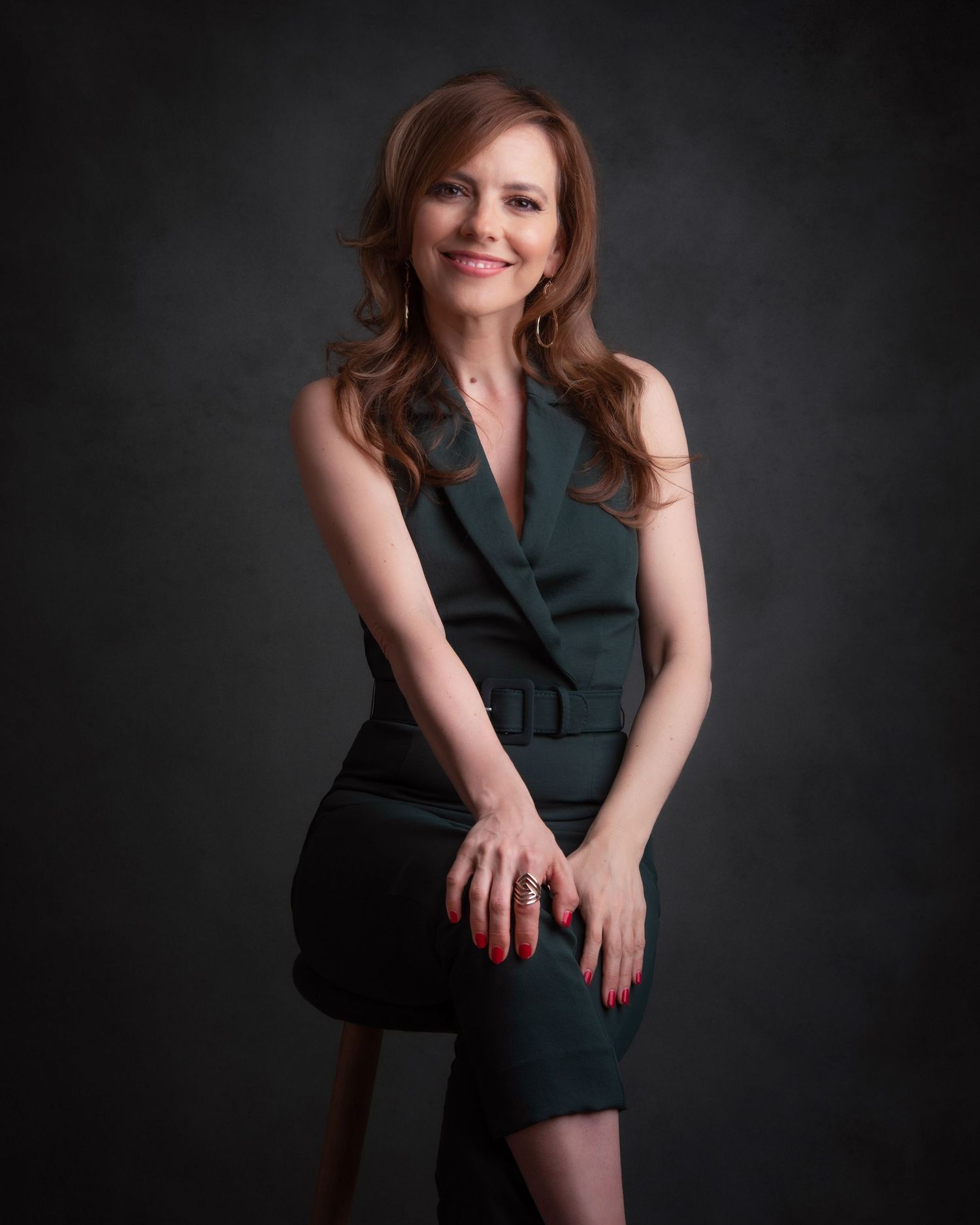 Professional studio portrait of a person wearing a sleeveless dark dress against a dramatic dark background.