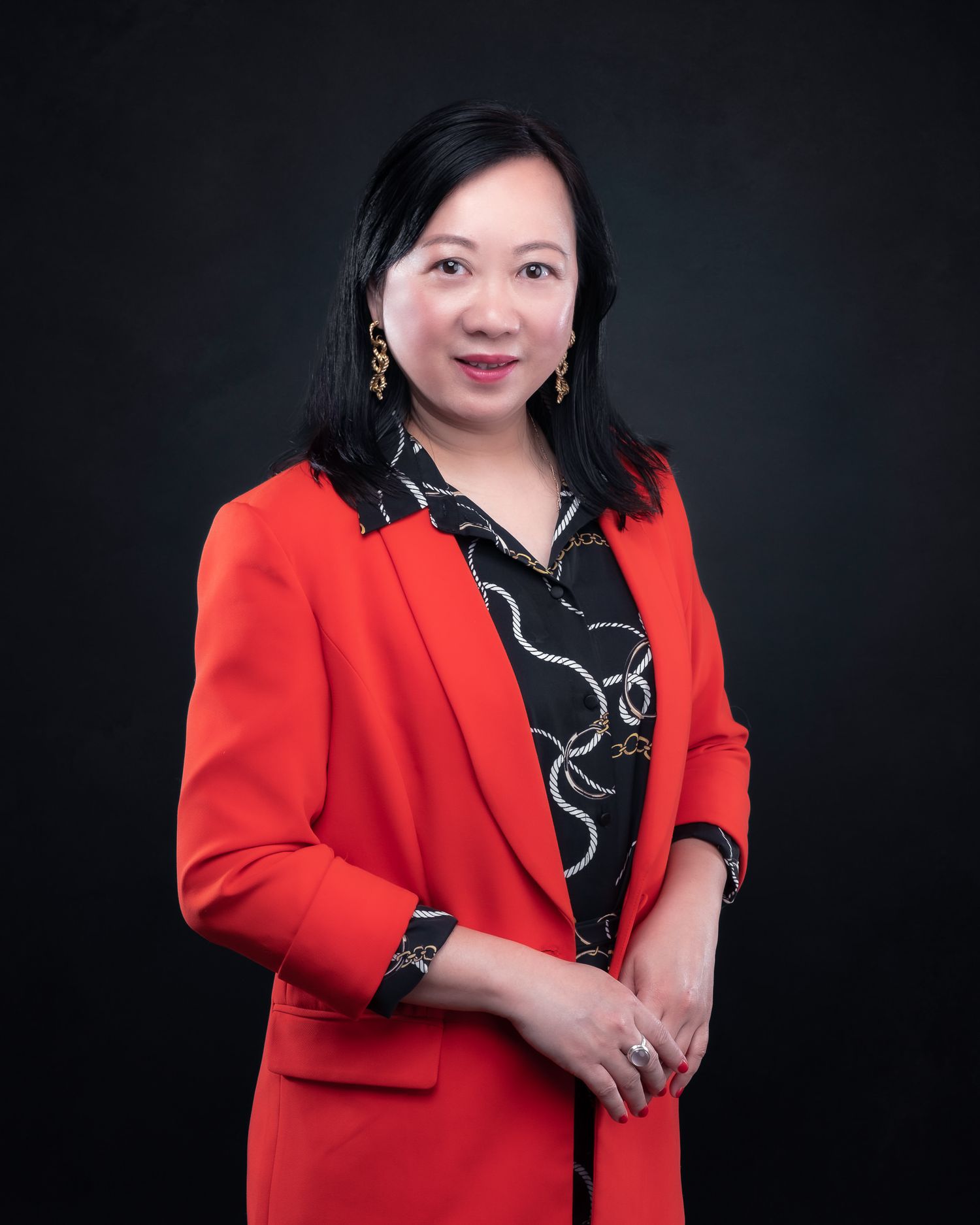 Professional studio portrait showing a person in a vibrant red blazer and patterned black blouse against a dark background.