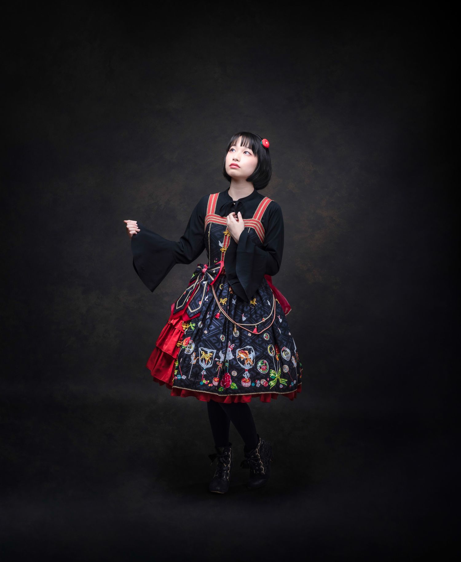 Figure in dark and red lolita fashion dress with floral patterns poses dramatically against black background.
